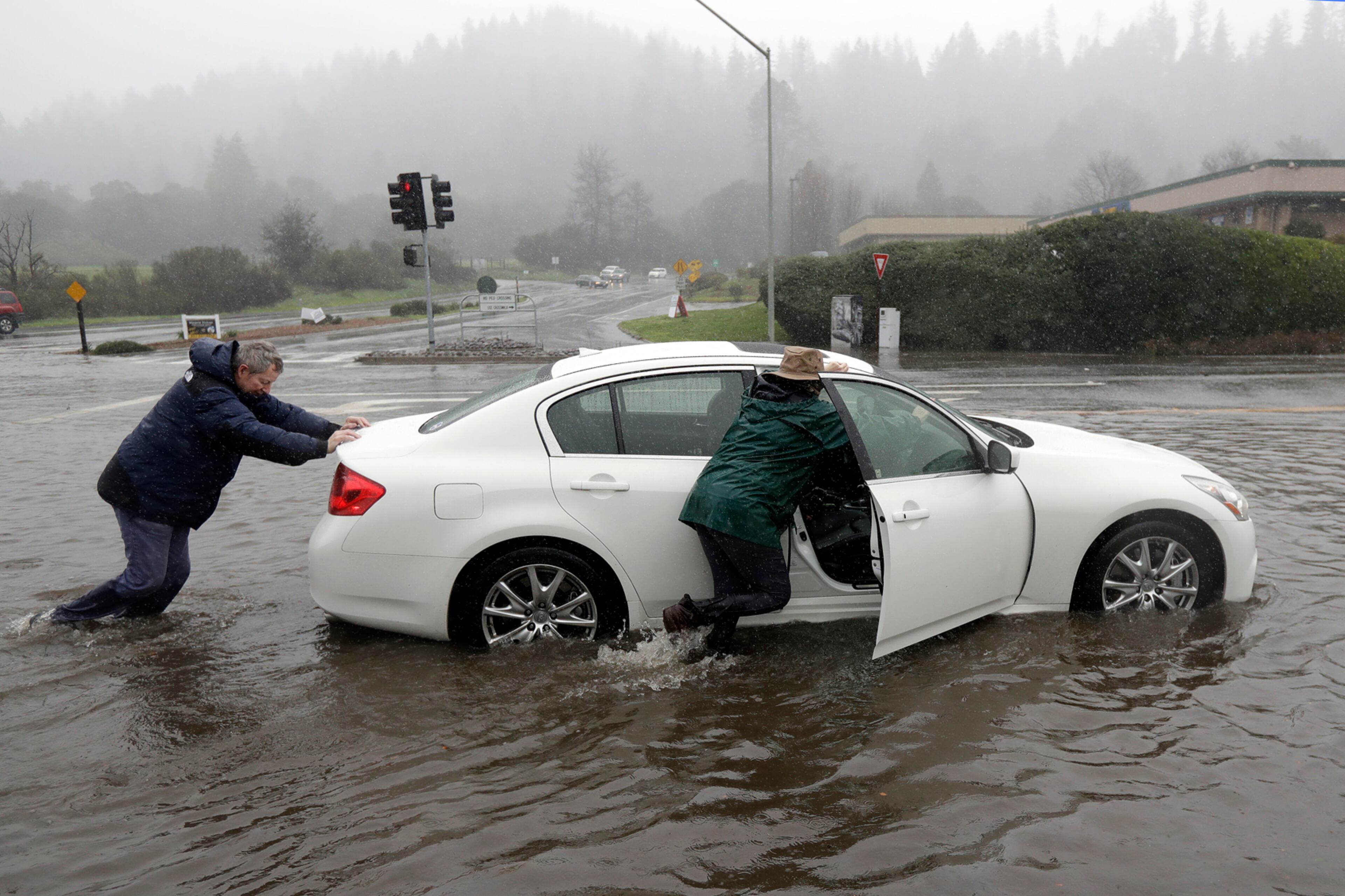 Terry Howard, left, pushes his stalled car from a flooded street with the help of his wife Janie Tuesday, Feb. 7, 2017, in Felton, Calif. Flash flood watches are in place for parts of Northern California down through the Central Coast as heavy rains swamp roads and threaten to overtop rivers and creeks. (AP Photo/Marcio Jose Sanchez)
