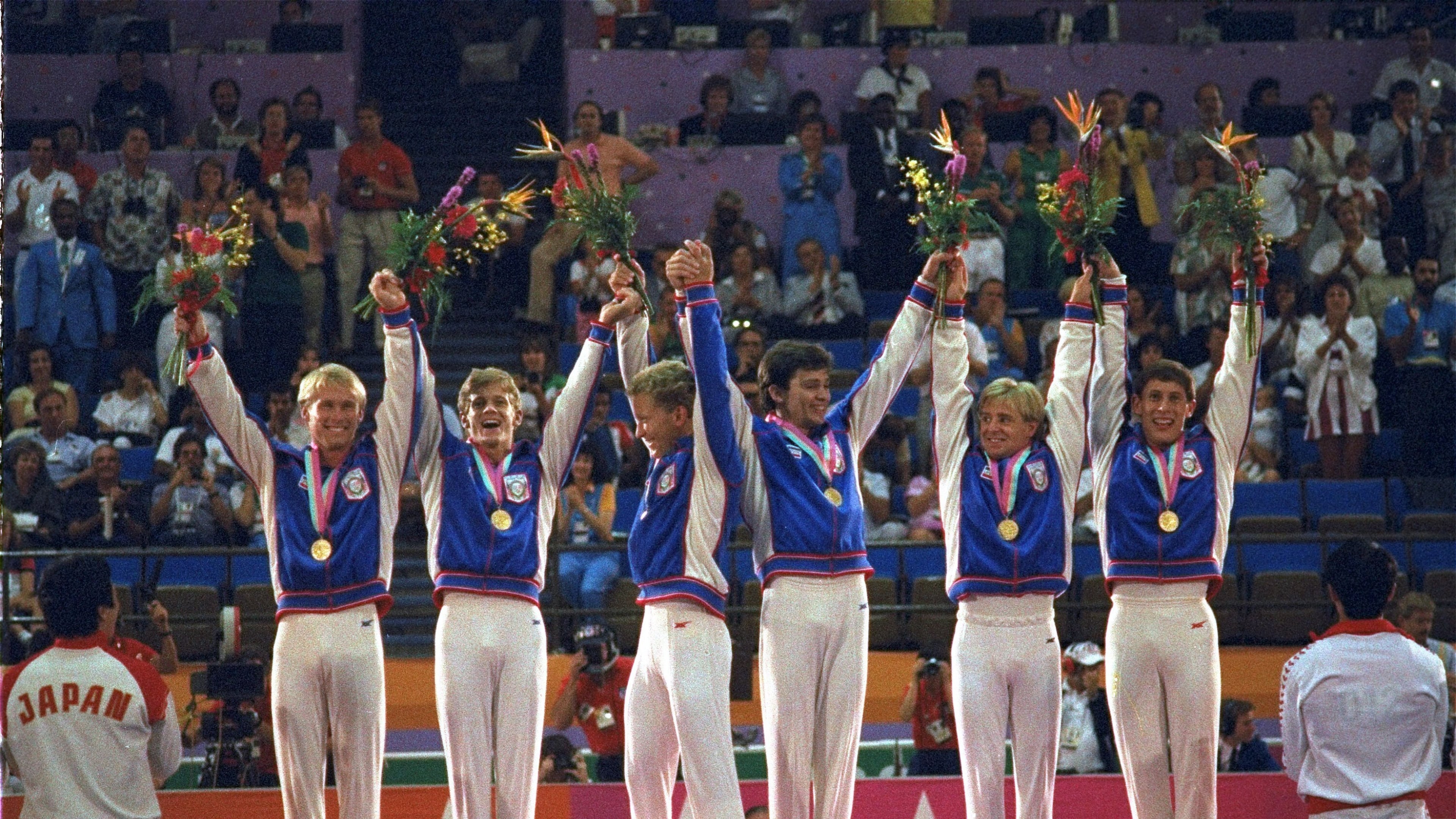 FILE - Members of the U.S. gymnastics team, from left: Bart Conner, Peter Vidmar, Jim Hartung, Mitch Gaylord, Scott Johnson and Tim Daggett, celebrate their gold medals as they stand on the winners' platform July 31, 1984 after they defeated world champion China to win the first U.S. gold medal in gymnastics in 80 years. (AP Photo/Lionel Cironneau, file)