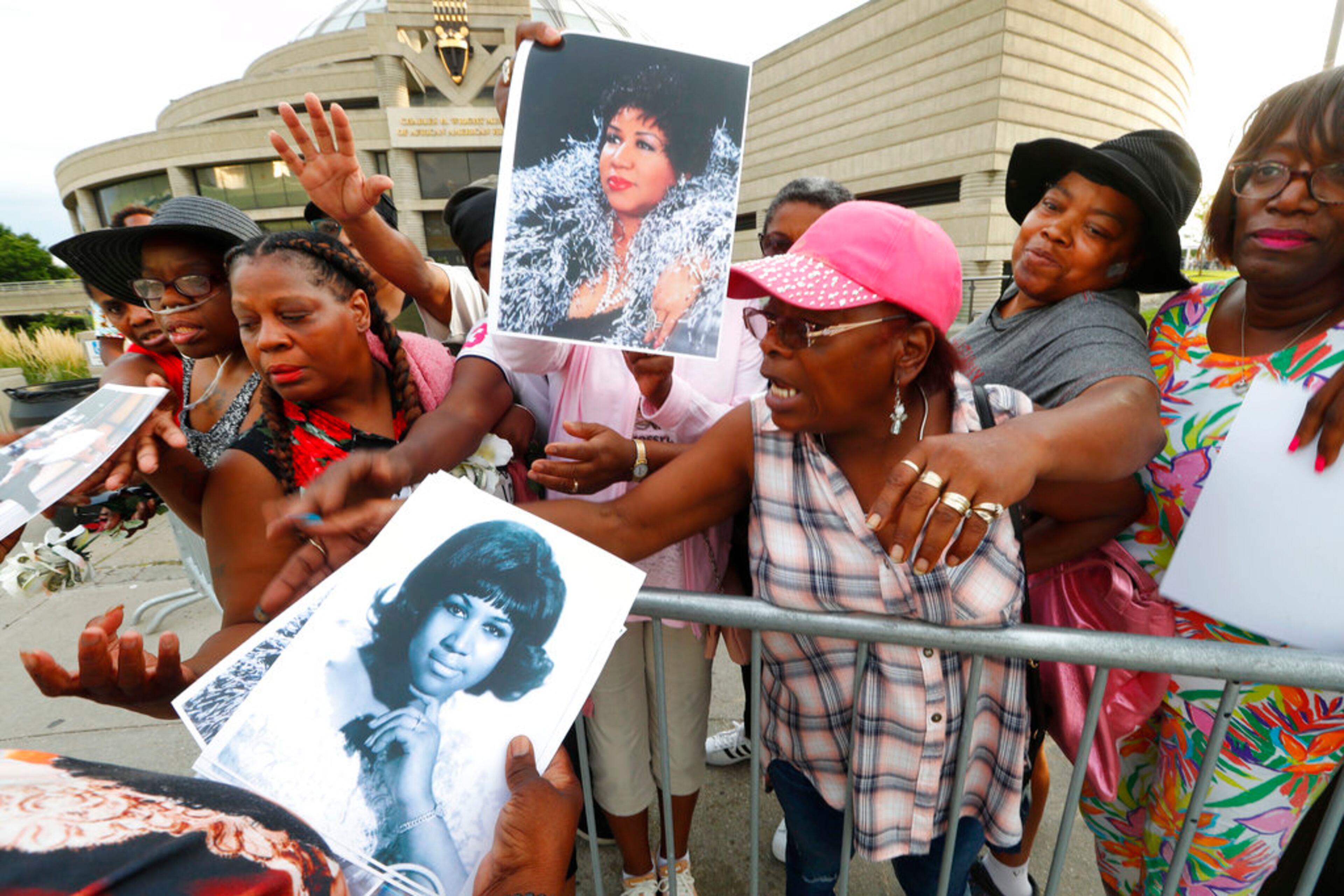People in line reach for photos being handed out outside the Charles H. Wright Museum of African American History during a public visitation for Aretha Franklin in Detroit, Wednesday, Aug. 29, 2018. Franklin died Aug. 16, of pancreatic cancer at the age of 76. (AP Photo/Paul Sancya)