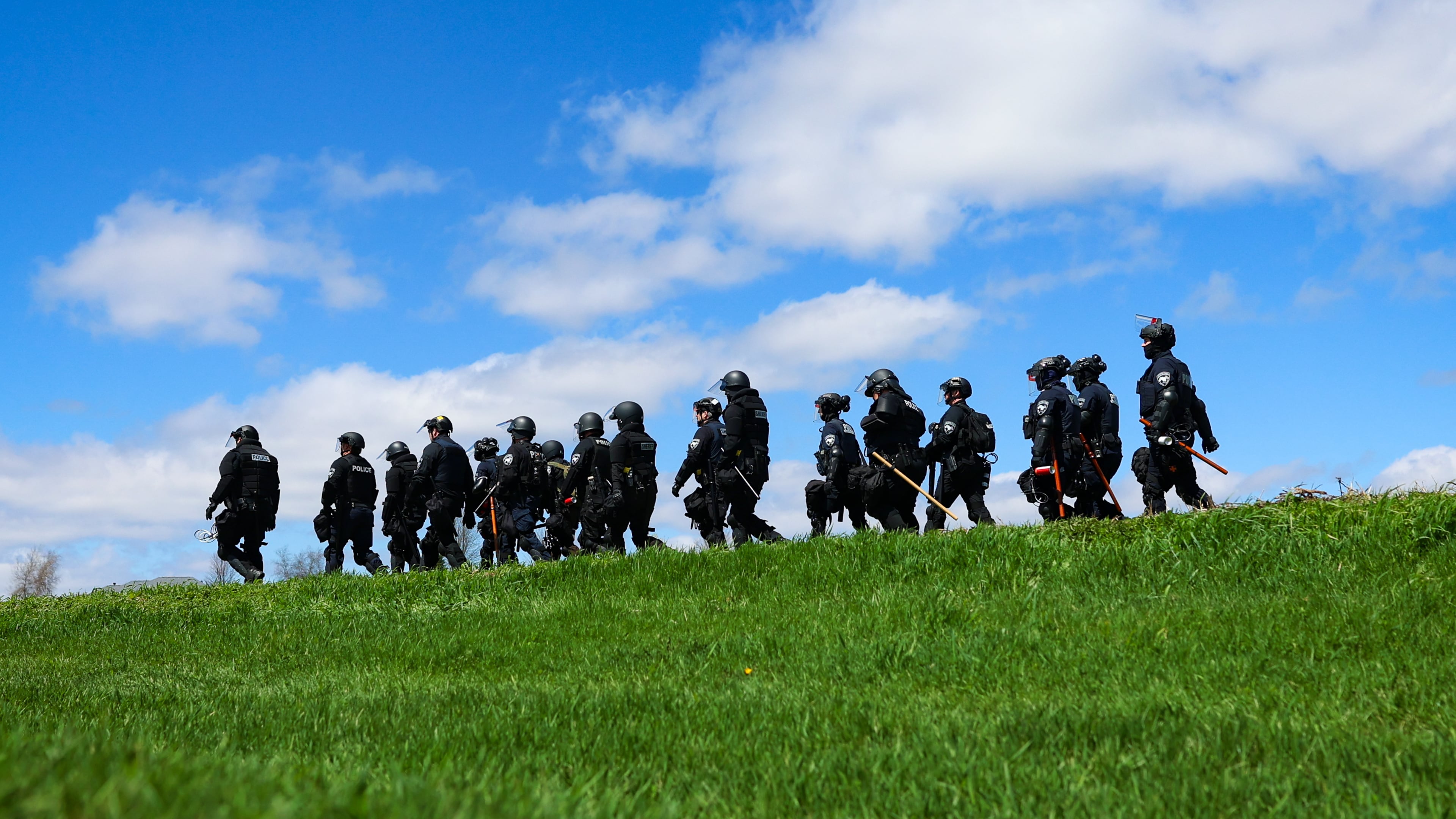 Law enforcement in riot gear walk in a field after animal welfare activists attempted to gain entry to Ridglan Farms beagle breeding and research facility on Saturday, April 18, 2026, in Blue Mounds, Wis. (Owen Ziliak/Wisconsin State Journal via AP)