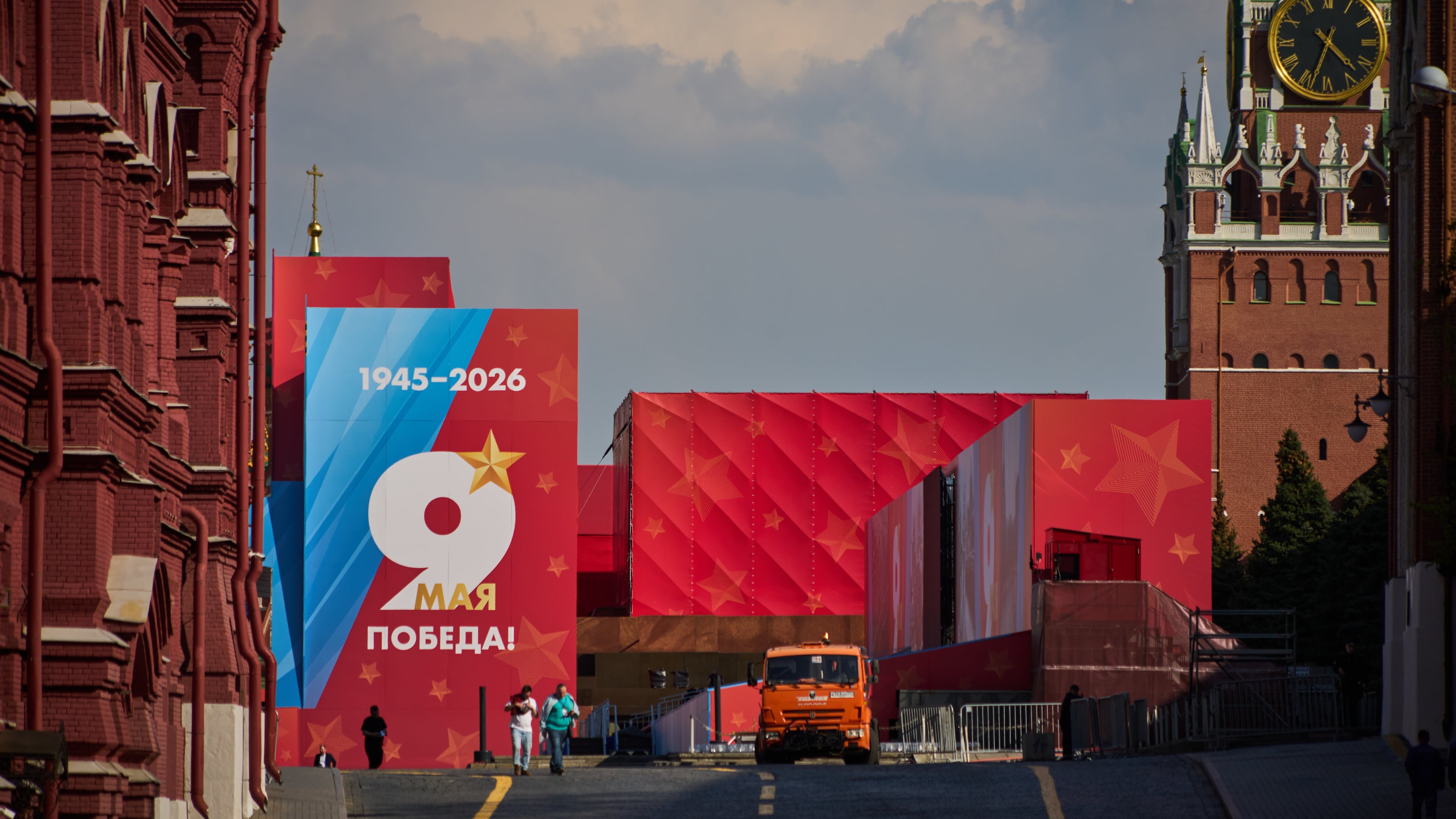 People walk in front of Victory Day poster walking from closed for entry Red Square decorated for the celebrations of the 81st anniversary of the Soviet Union's victory over Nazi Germany during World War II, in Moscow, on Wednesday, May 6, 2026, backdropped by the Spasskaya Tower on the right. (AP Photo/Alexander Zemlianichenko)