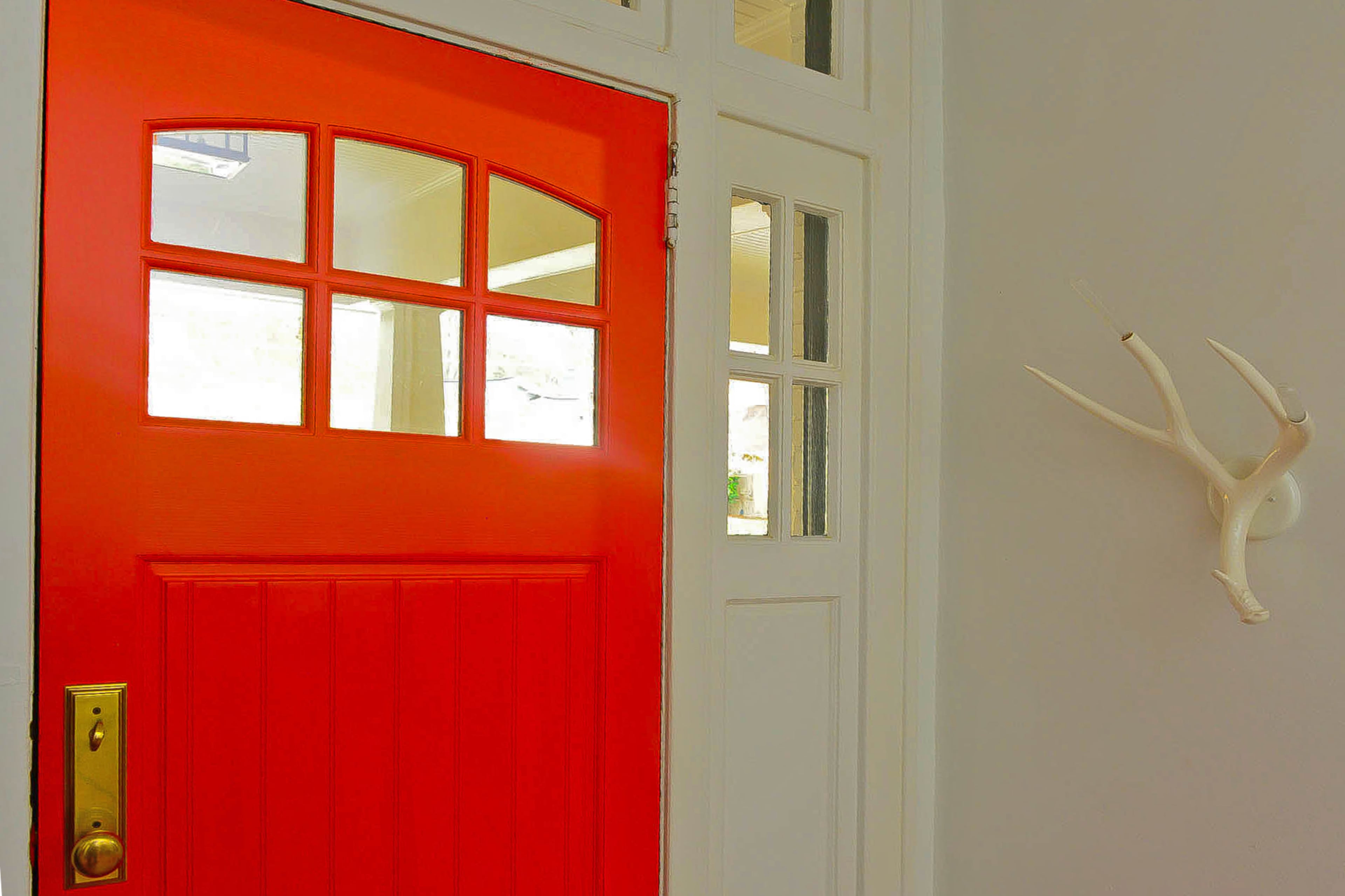 A neon coral door and white antler sconce from Roll & Hill provide a radiant welcome in the entryway of the Craftsman-style home.