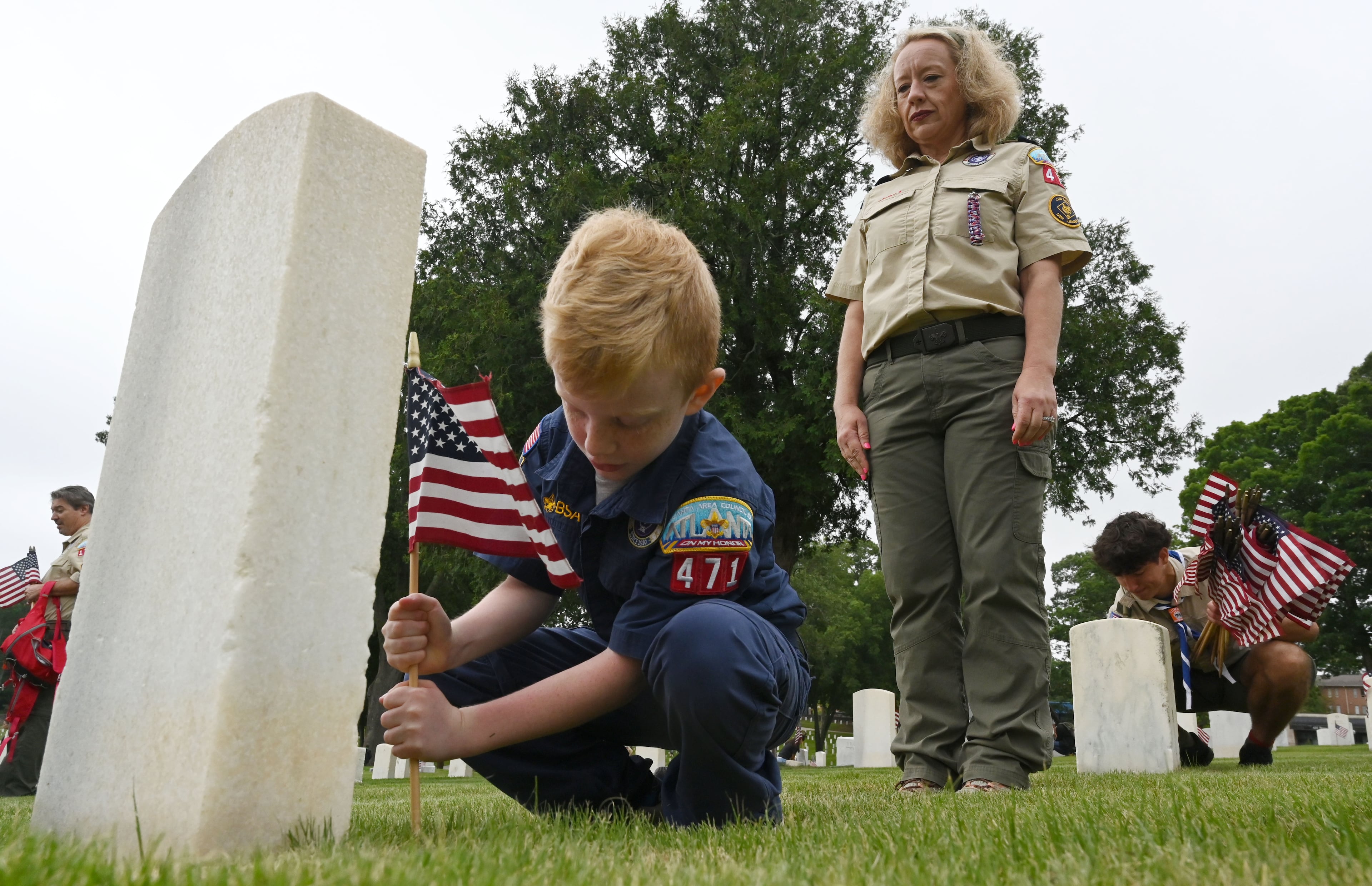 Cade Larkin, 9, places a flag as his mother, Ingle Larkin, looks on during the Memorial Day Flag Placement event at Marietta National Cemetery on Saturday, May 23, 2026, in Marietta. Scouting groups in the community place more than 18,000 U.S. veteran grave flags at Marietta National Cemetery each year on the Saturday before Memorial Day, helping prepare for Monday’s ceremony. The long-running service project—organized with the National Memorial Day Association of Georgia—also gives youth and adults an opportunity to honor fallen service members and learn about their sacrifices and the area’s history. (Hyosub Shin/AJC)