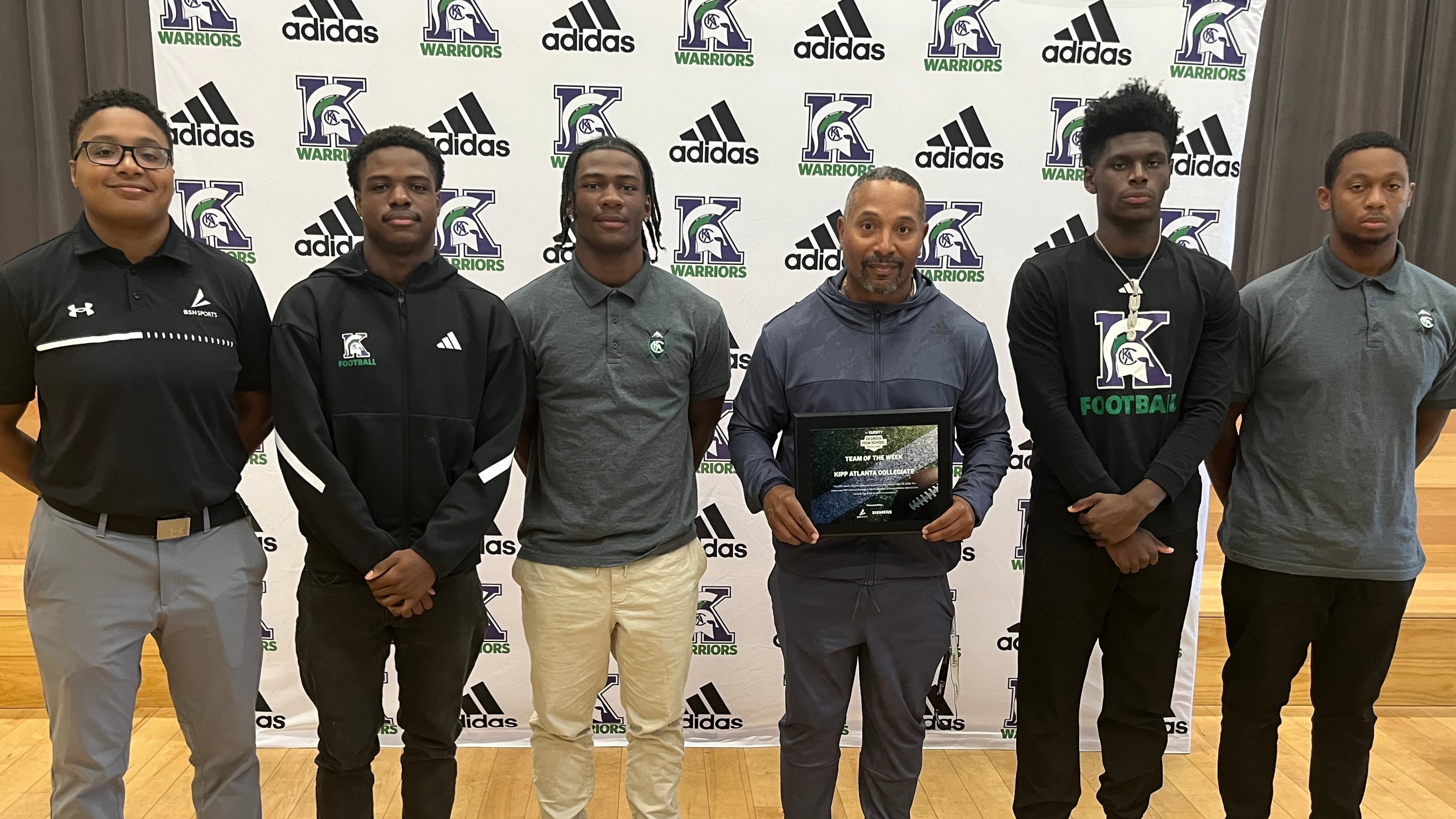 KIPP Atlanta Collegiate coach Corey Jarvis (fourth from left) accepts the award for AJC Varsity Team of the Week after his Warriors beat Lovett 34-0 on Friday, Sept. 25, 2026. Also pictured are Erin Kelley (left) of award sponsor BSN Sports and KIPP Atlanta captains Travion Callaway (second from left), Dylan Favors (third from left), LaDell Moreland (second from right) and Kris McMichael.