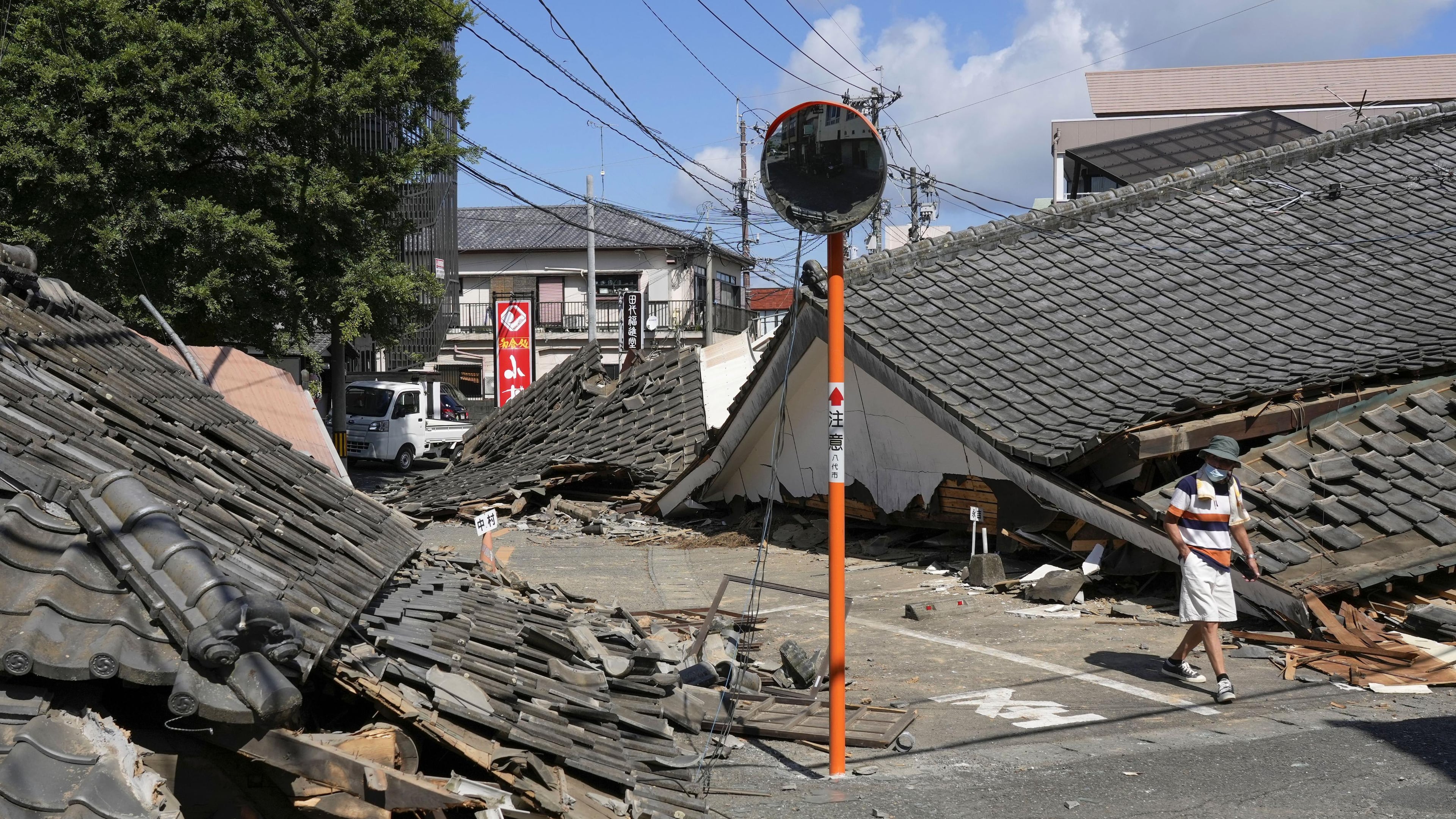 A person walks past the houses collapsed in an earthquake in Yatsushiro, Kumamoto Prefecture, southern Japan, Friday, July 31, 2026. (Koji Harada/Kyodo News via AP)