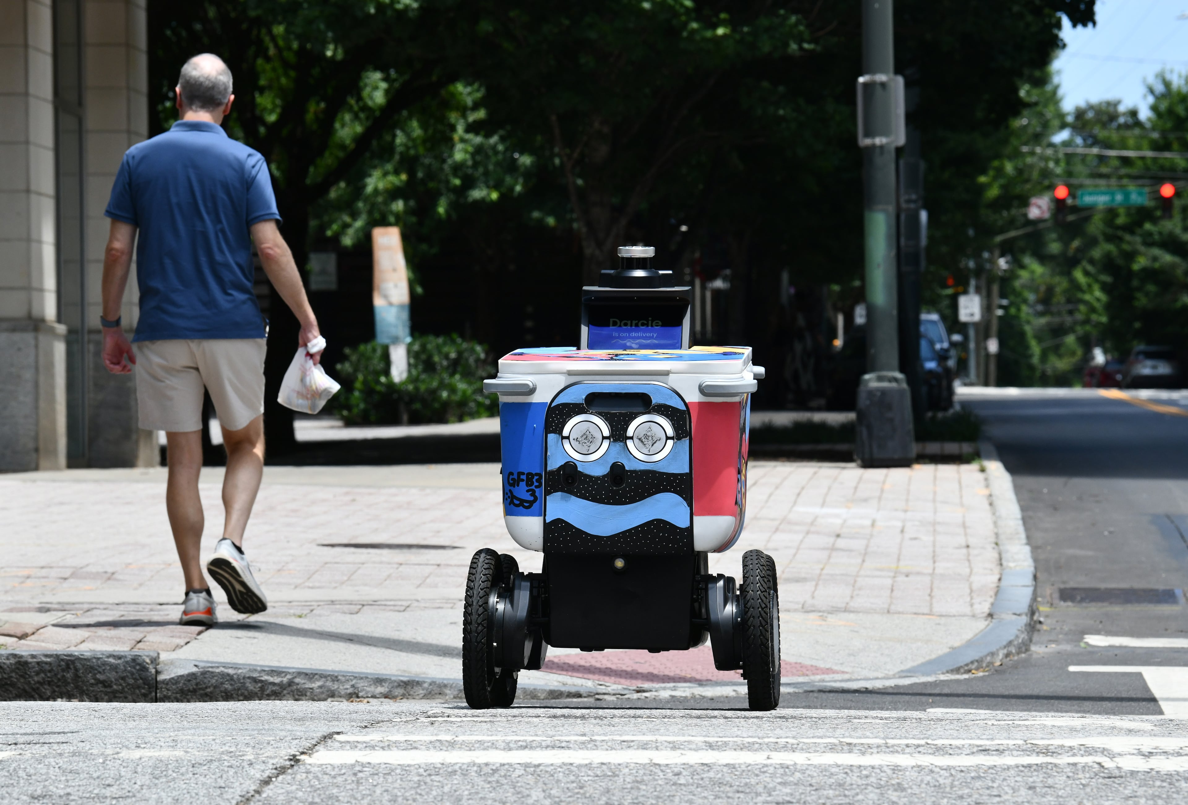 A pedestrian shares the sidewalk with a food delivery robot in Atlanta. (Hyosub Shin/AJC)