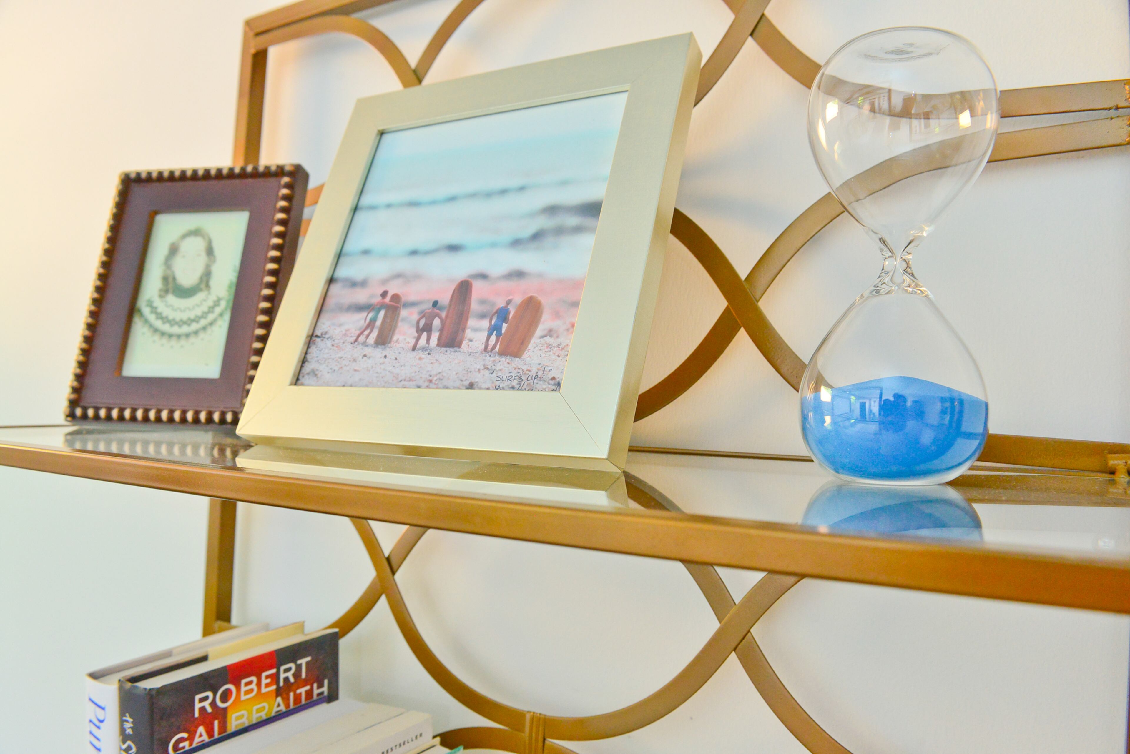A gold shelf from Westside Market Antiques and Interiors in Atlanta holds favorite photos, knickknacks and books. The blue sand hourglass and framed photograph of surfers are nods to the coastal interior design found throughout the bungalow.