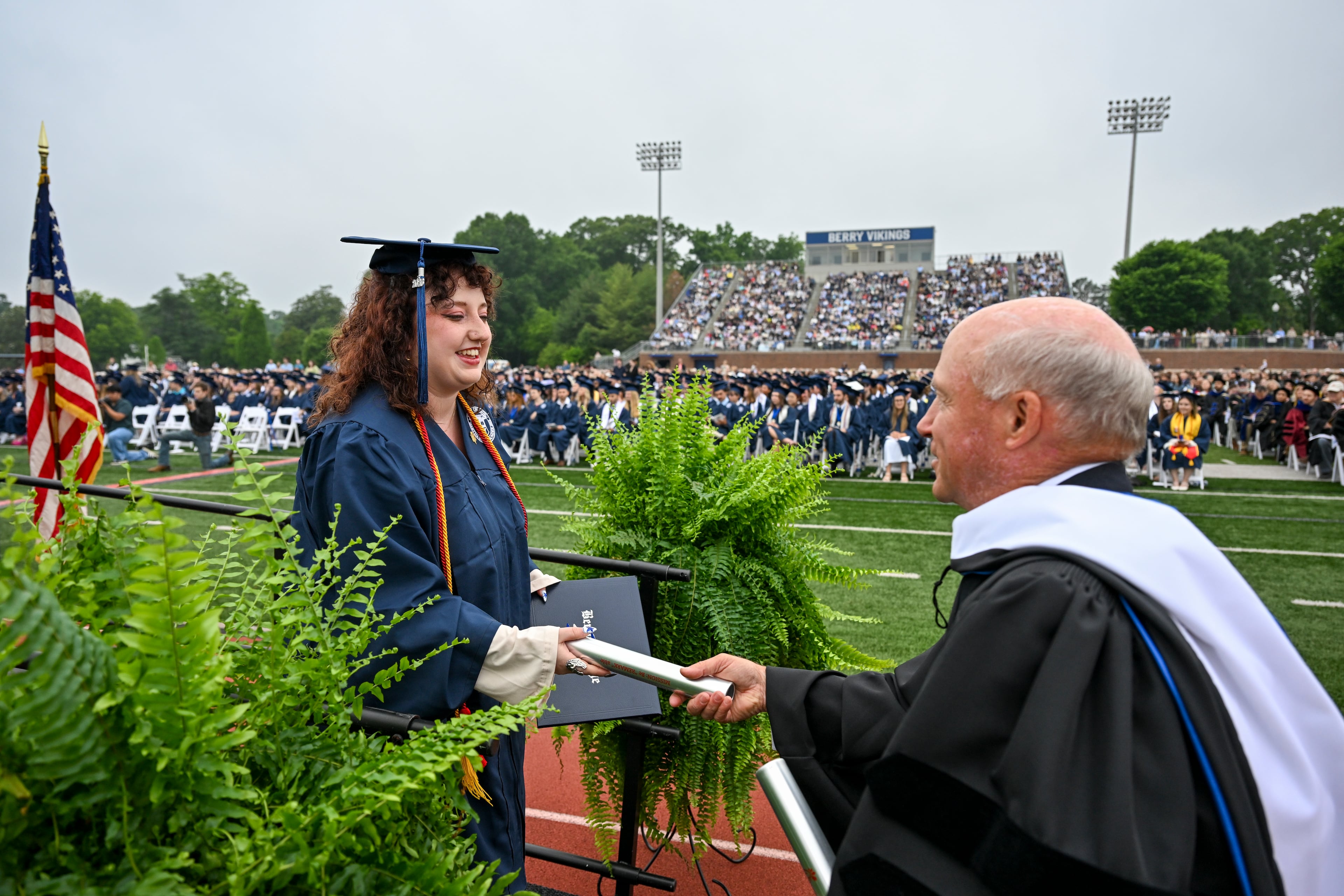 Berry College graduate Caron Bonner receives a relay baton from Dan Cathy, chairman of Chick-fil-A, during commencement on Saturday, May 9, 2026. Cathy, who served as the featured speaker, presented each graduate with a relay baton. Using the baton as part of his address, Cathy compared graduation to a relay race, reminding students that many people helped carry them to this moment and encouraging them not to "drop the baton" as they move into the next chapter of life. (Brant Sanderlin/Berry College)