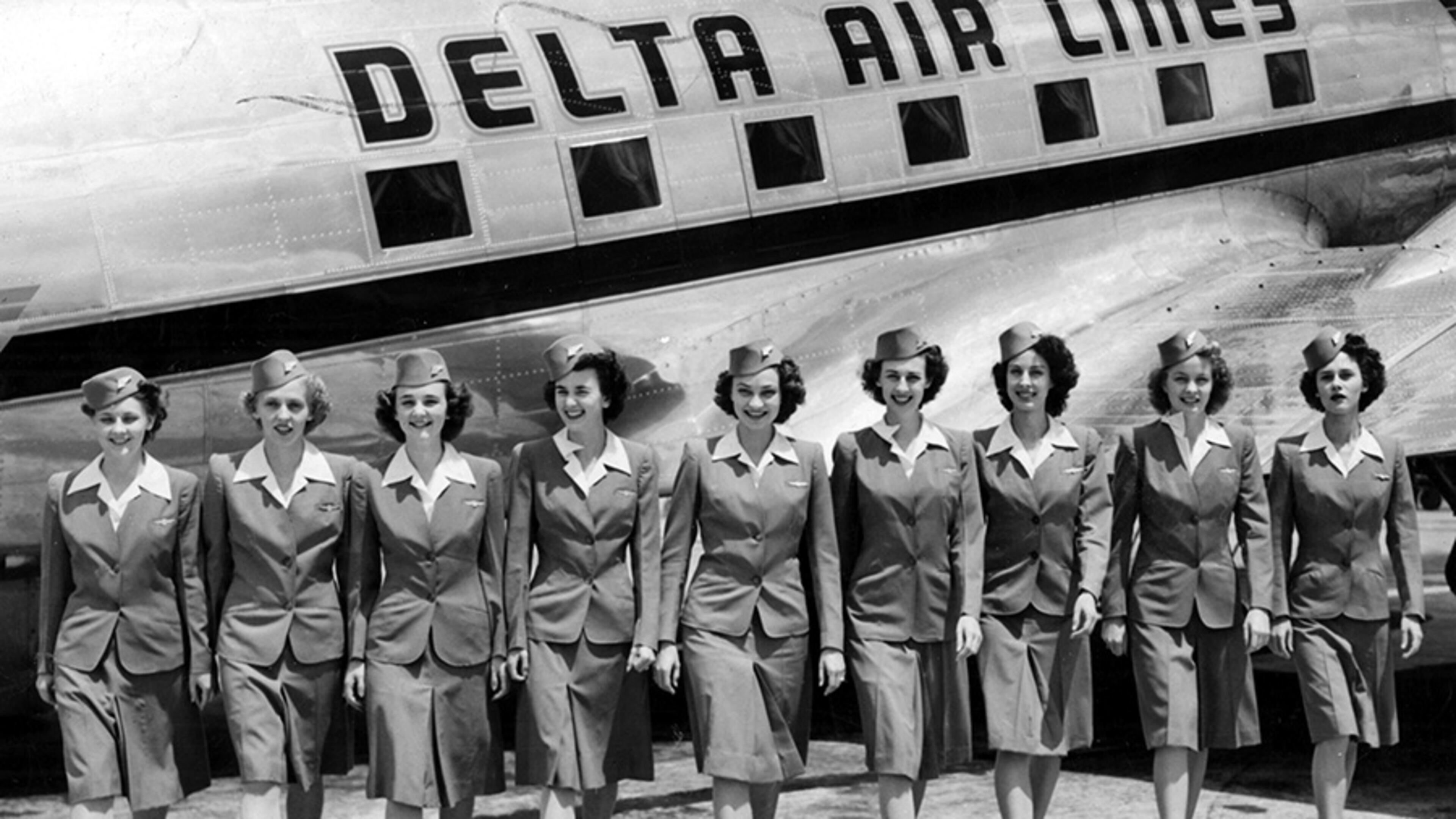 1945 -- Nine of Delta's flying beauties shown beside a big transport on the apron of the Atlanta Airport. From left to right: Isabel Sanders, Martha Watkins, Josephine Pate, Alberta Cason, Frances Cooper, Christine Ferguson, Hedy Swindel, Nora Walsh and Virginia Lewis.