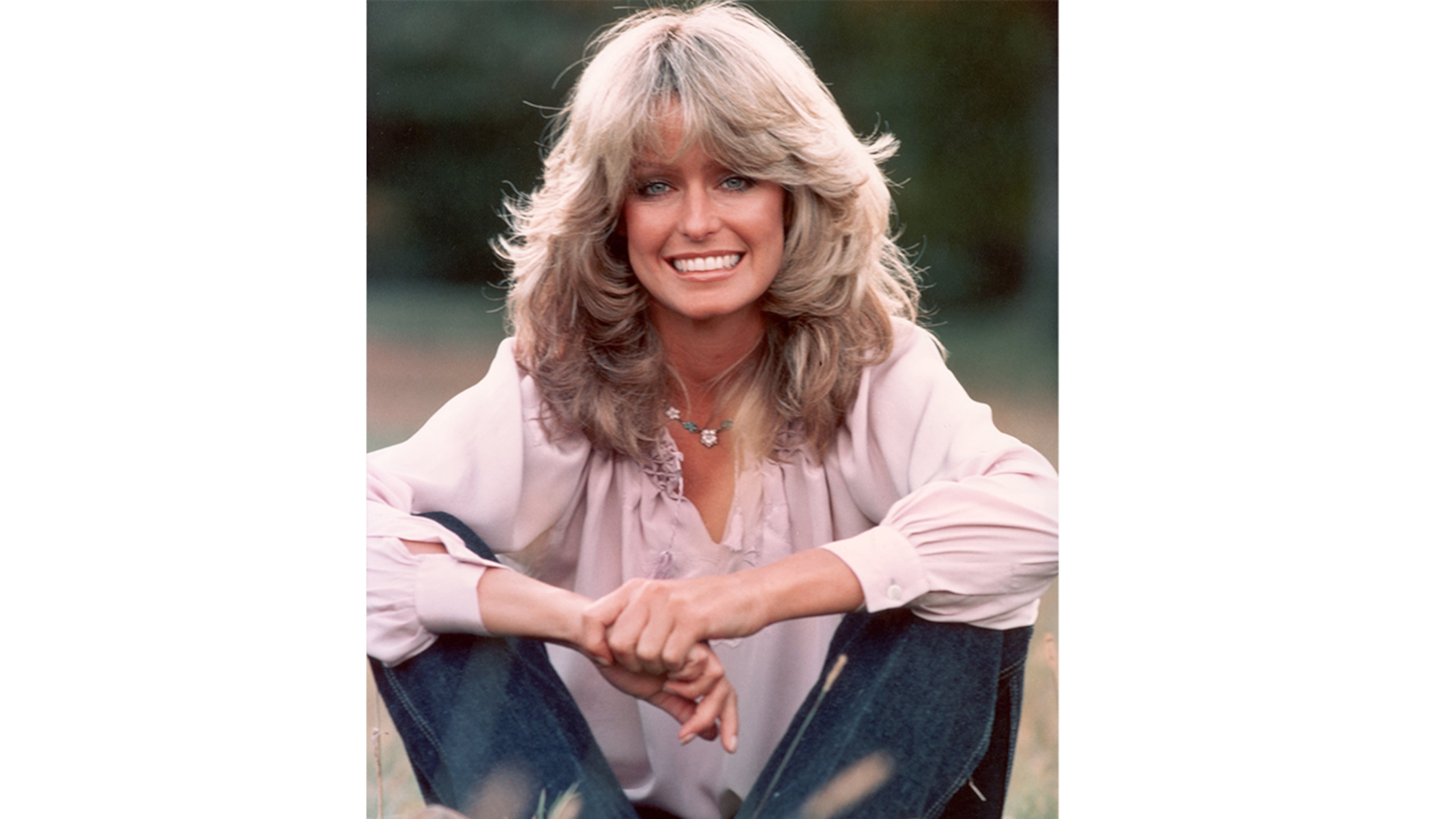 Publicity portrait of American actor and model Farrah Fawcett smiling while sitting outdoors in blue jeans and a mauve blouse. (Photo by Hulton Archive/Getty Images)