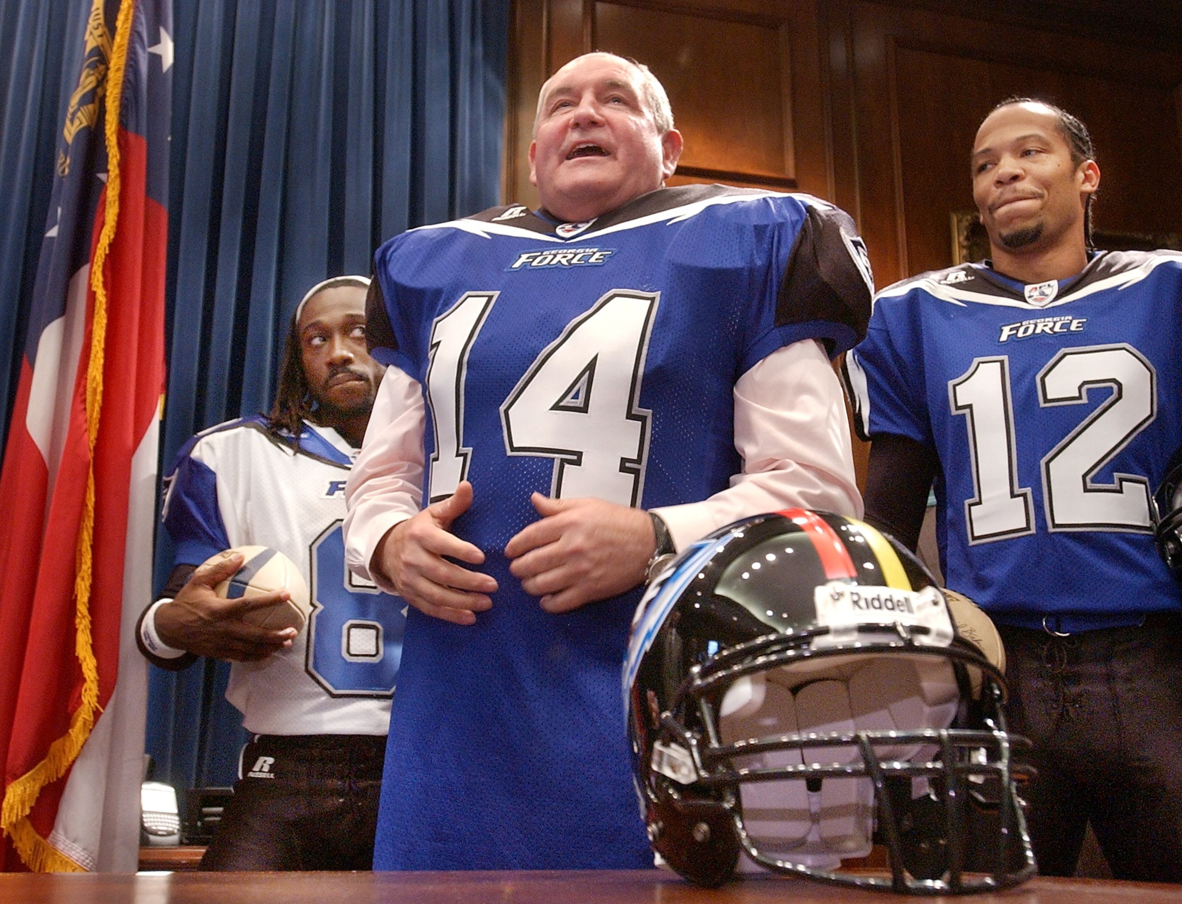 040127 - ATLANTA, GA -- Gov. Sonny Perdue cq models the new Georgia Force football jersey and pads as part of a photo opporunity at the capitol on Tuesday, January 27, 2002, to promote the Arena Football team's upcoming third season. Behind Perdue are Force players Markeith Cooper (cq) (left) and Leon Murray (cq) (right). (RICH ADDICKS/AJC staff)