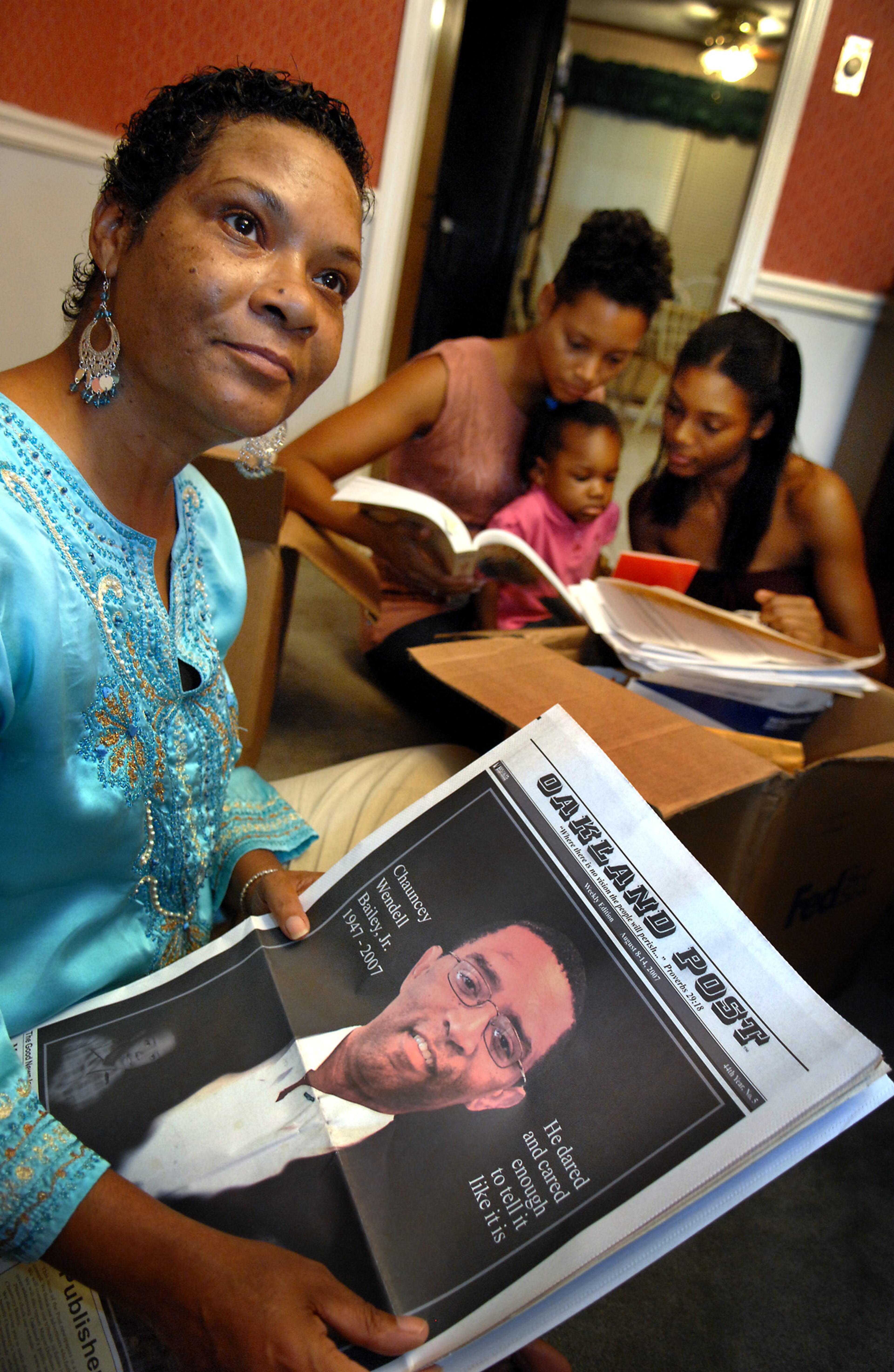 In this 2007 file photo, Lorelei Waqia (left) of Lithonia, Ga., holds a copy of an Oakland Post newspaper with the picture of her brother, Chauncey Bailey, who was the paper's editor. Waqia recalled that her brother lived and breathed journalism, giving voice to those who had none and mentoring those who wanted to follow in his shoes, but then someone killed him. Also pictured are his nieces, Kareemah Iddeen and Sadiyyah Iddeen, as they look through some of his books. In their lap is two-year-old Sahriyah Anderson, Waqia's granddaughter. Bailey was shot dead in 2007 on an Oakland street. Two men associated with an Oakland-area bakery that Bailey had been investigating were later convicted of ordering the killing. A third man confessed to being the triggerman.