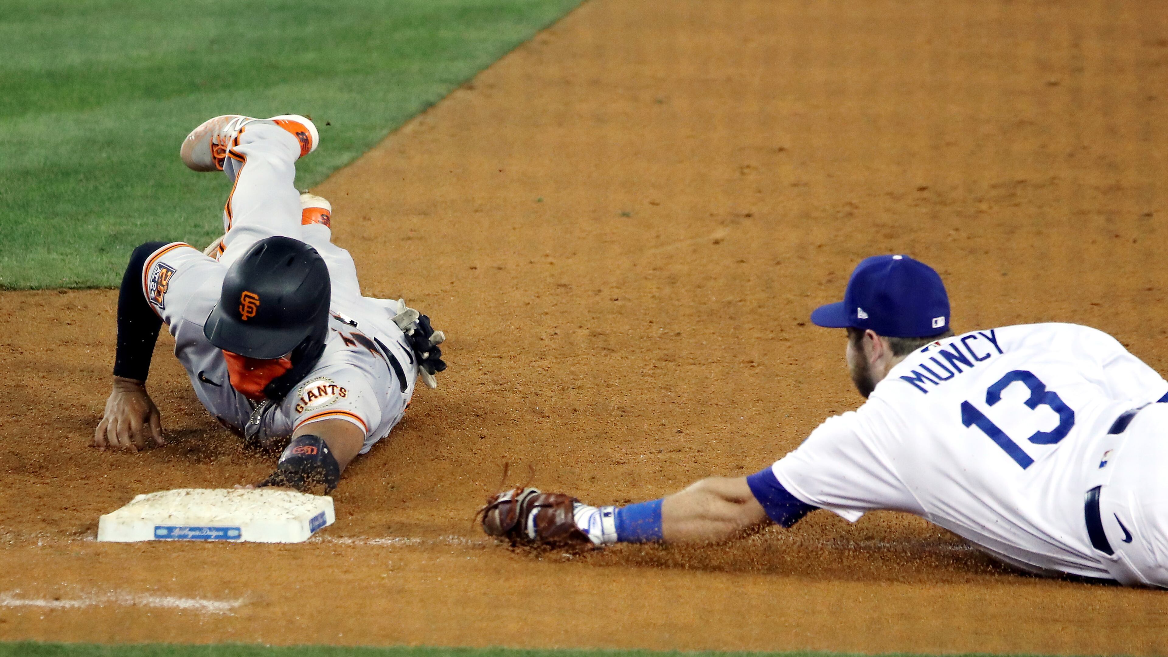 The San Francisco Giants' Chadwick Tromp slides back to first base as Los Angeles Dodgers first baseman Max Muncy (13) tries to catch him off the bag during the seventh inning at Dodger Stadium in Los Angeles on Friday, Aug. 7, 2020. The Dodgers won, 7-2. (Katelyn Mulcahy/Getty Images/TNS)
