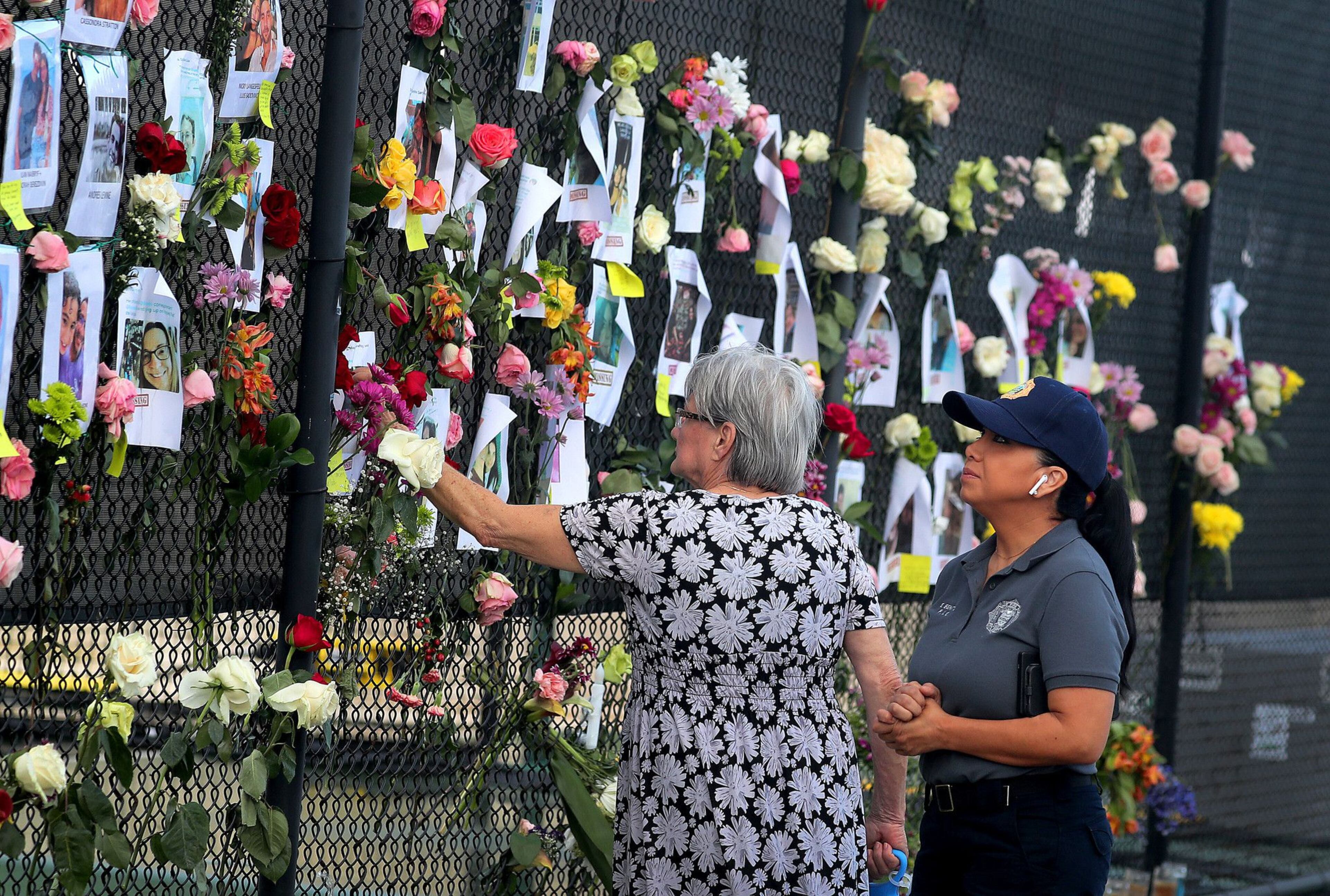 Maria Rosa Perez, a neighbor and Erika Benitez with Miami Date Fire Rescue pause to look over the names and faces of some of the people missing on Saturday June 26, 2021. The on a makeshift memorial is across the street from the site of the 12-story oceanfront Champlain Towers South Condo, at 8777 Collins Ave., that partially collapsed around 2 a.m. on Thursday, June 24, 2021 in Surfside, Fl.