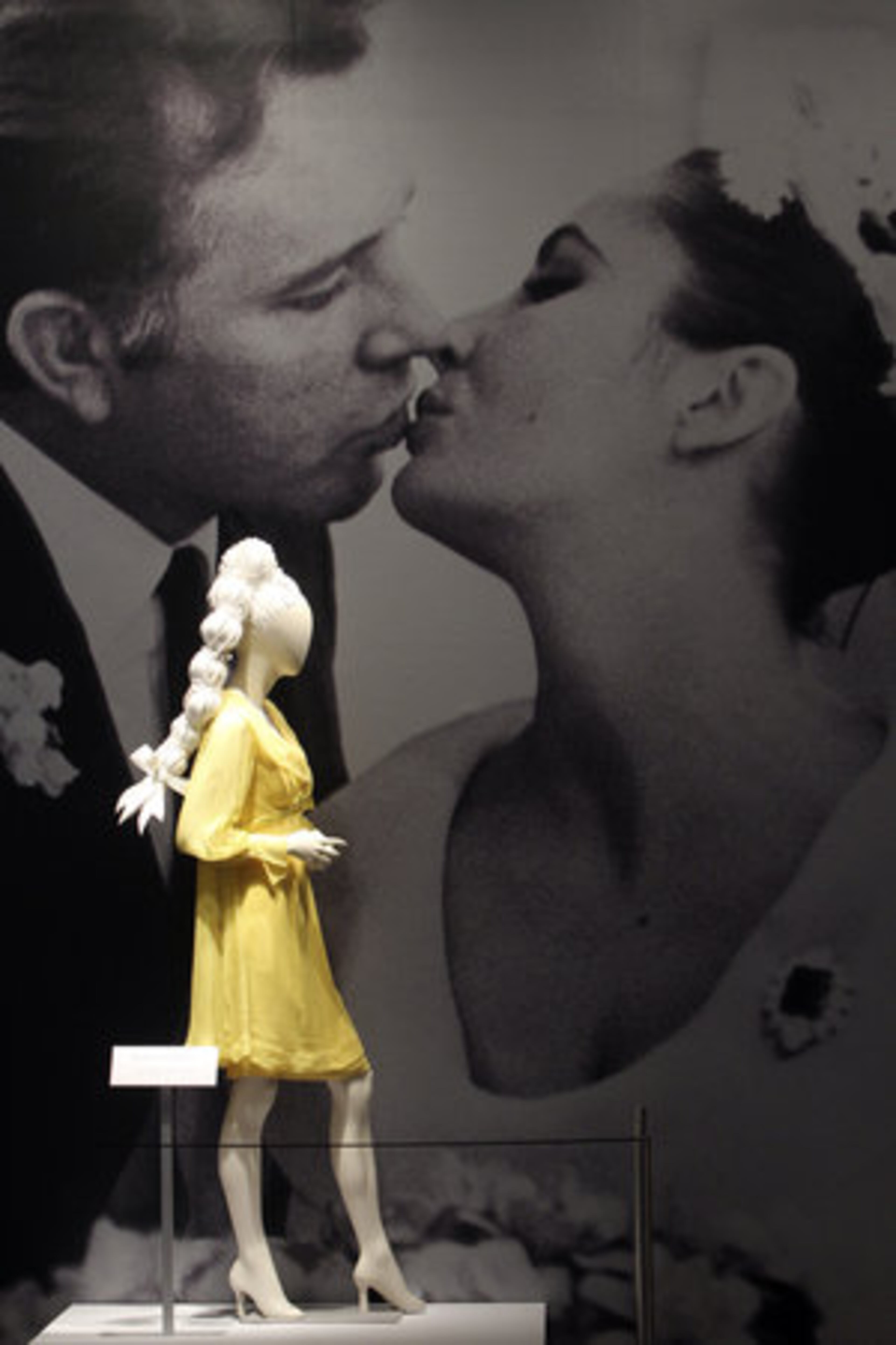 A Sunflower Yellow Chiffon wedding dress for her first marriage to Richard Burton is displayed in front of a photo from the wedding day.