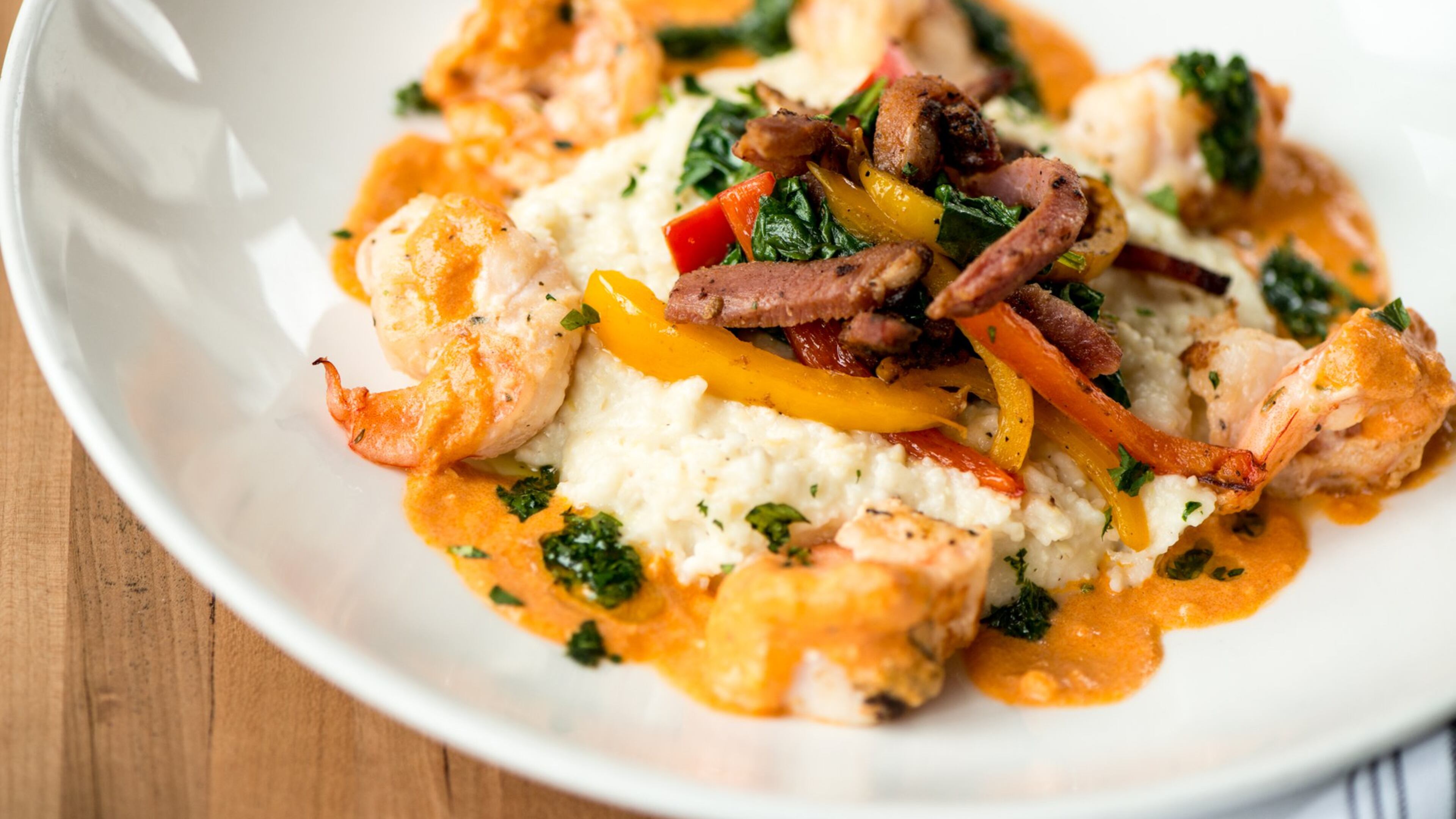 Camps Kitchen & Bar shrimp and grits with creamy cheese grits, spinach, tasso ham, bell peppers, and smoked tomato cream. Photo credit- Mia Yakel.