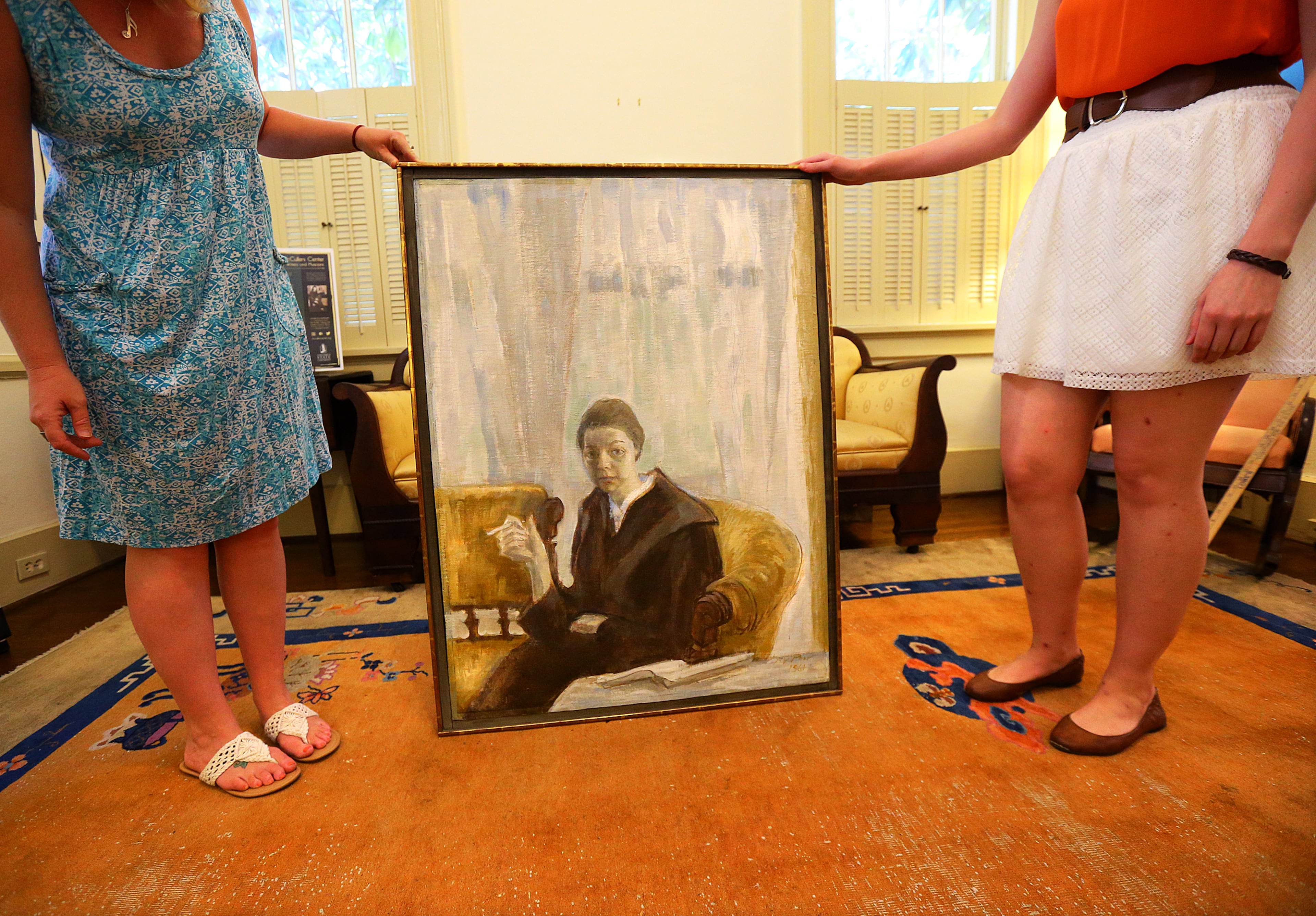 Director Courtney George (left) and student assistant Lauren Cantrell prepare to hang a 1961 painting of Carson McCullers by Henry Varnum Poor in the Smith-McCullers House Museum on Tuesday, July 8, 2014, in Columbus. CURTIS COMPTON / CCOMPTON@AJC.COM