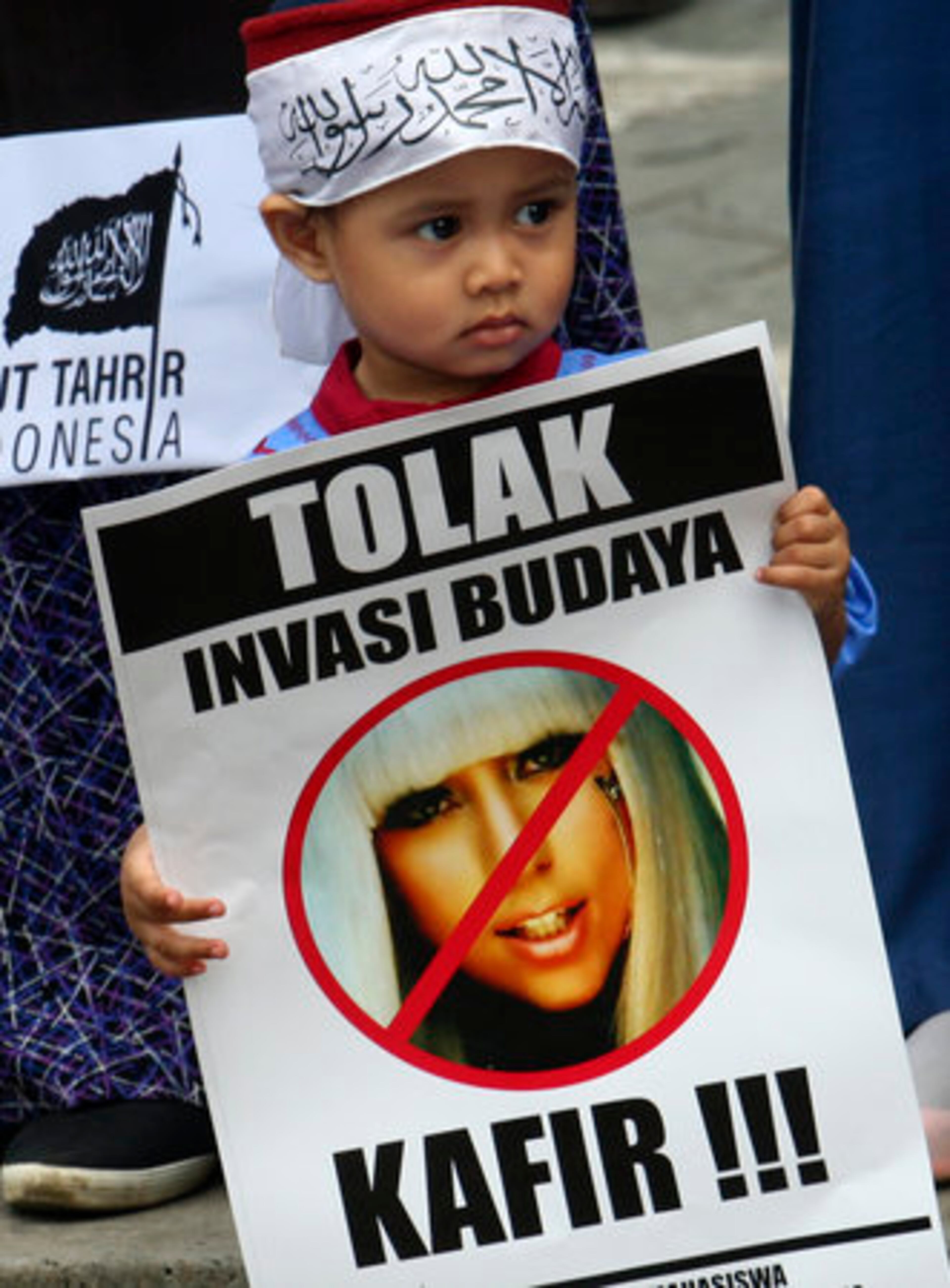 A Muslim boy holds a poster bearing a defaced picture of U.S. pop singer Lady Gaga during a protest against her concert. The writing on the poster reads "Reject cultural invasion" and "Infidel."