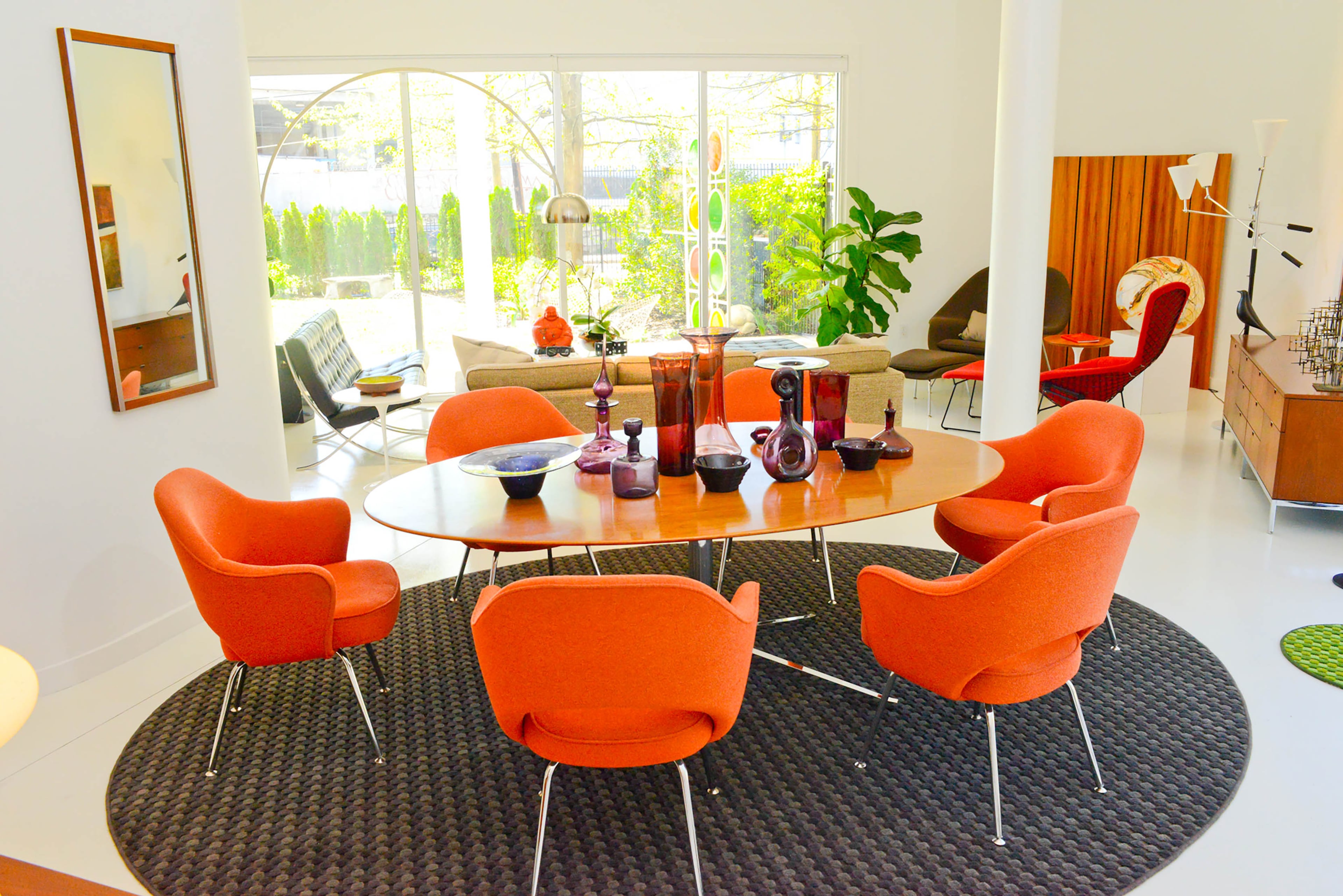 Orange chairs pop against the gray rug that anchors the dining room table. The rug, a custom piece from Myers Carpet of Atlanta, adds a touch of softness to balance the clean, white lines created by the epoxied floors, and painted concrete walls and ceilings.