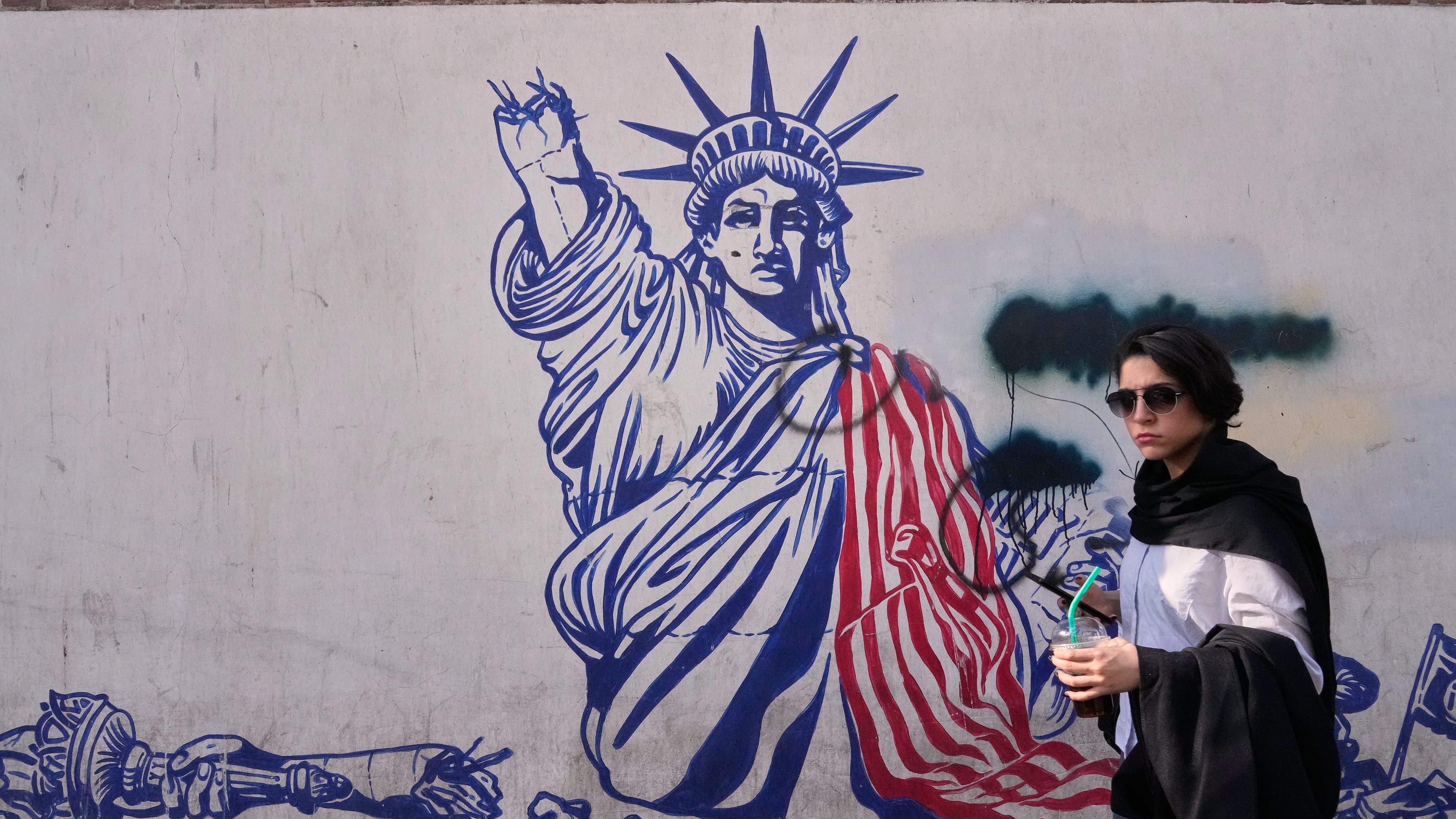 A woman walks past an anti-American mural on the wall of the former U.S. Embassy, now a museum, in Tehran, Iran, Friday, June 12, 2026. (AP Photo/Vahid Salemi)