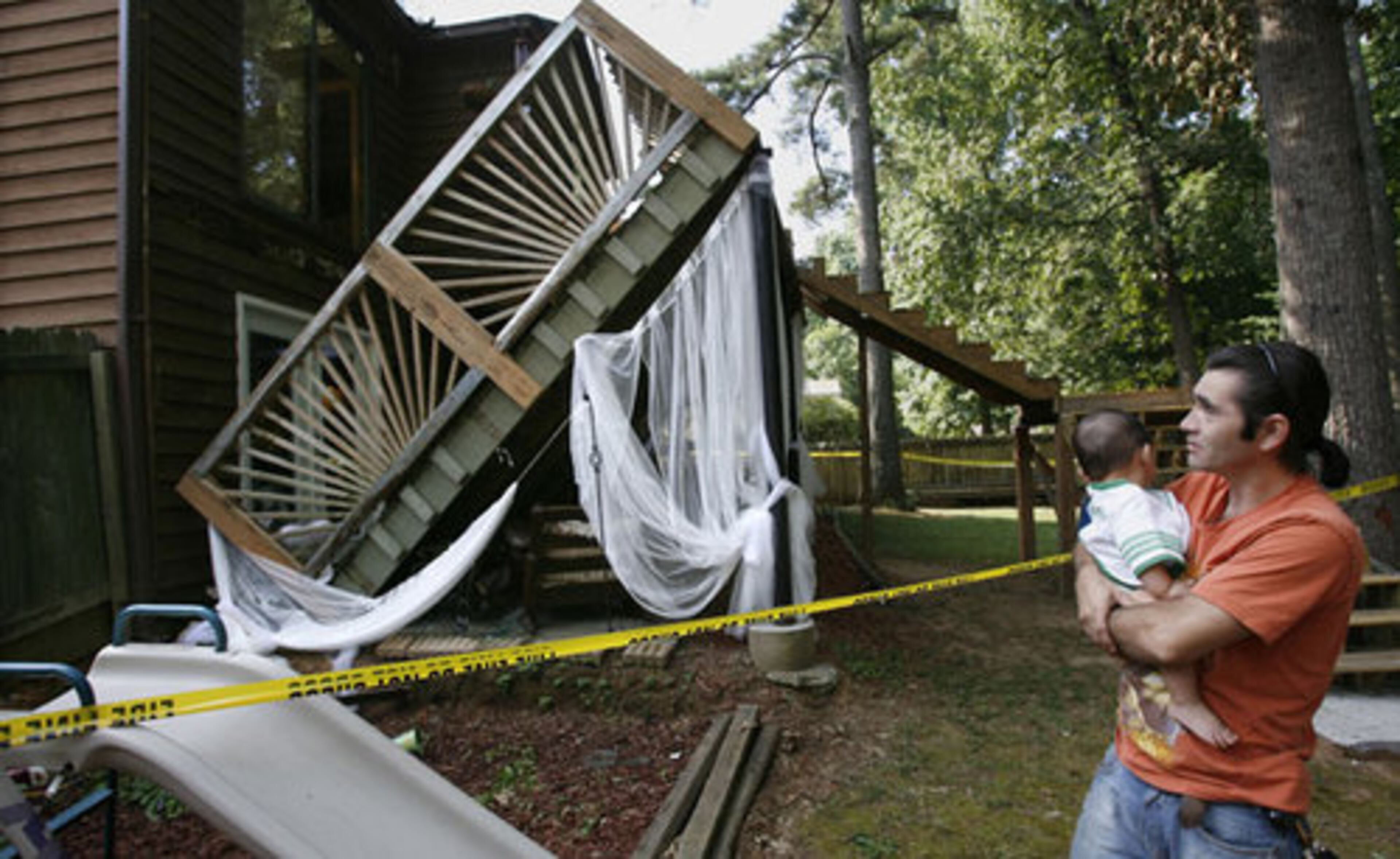 Ygor Zuniga, with his grandson, Adrian Medina, 6 months, checks out the deck that collapsed at the back of his Lawrenceville house. About 18 people were on the deck at the time, for a wedding party. Four children and one adult were treated at area hospitals for injuries that were not life-threatening.