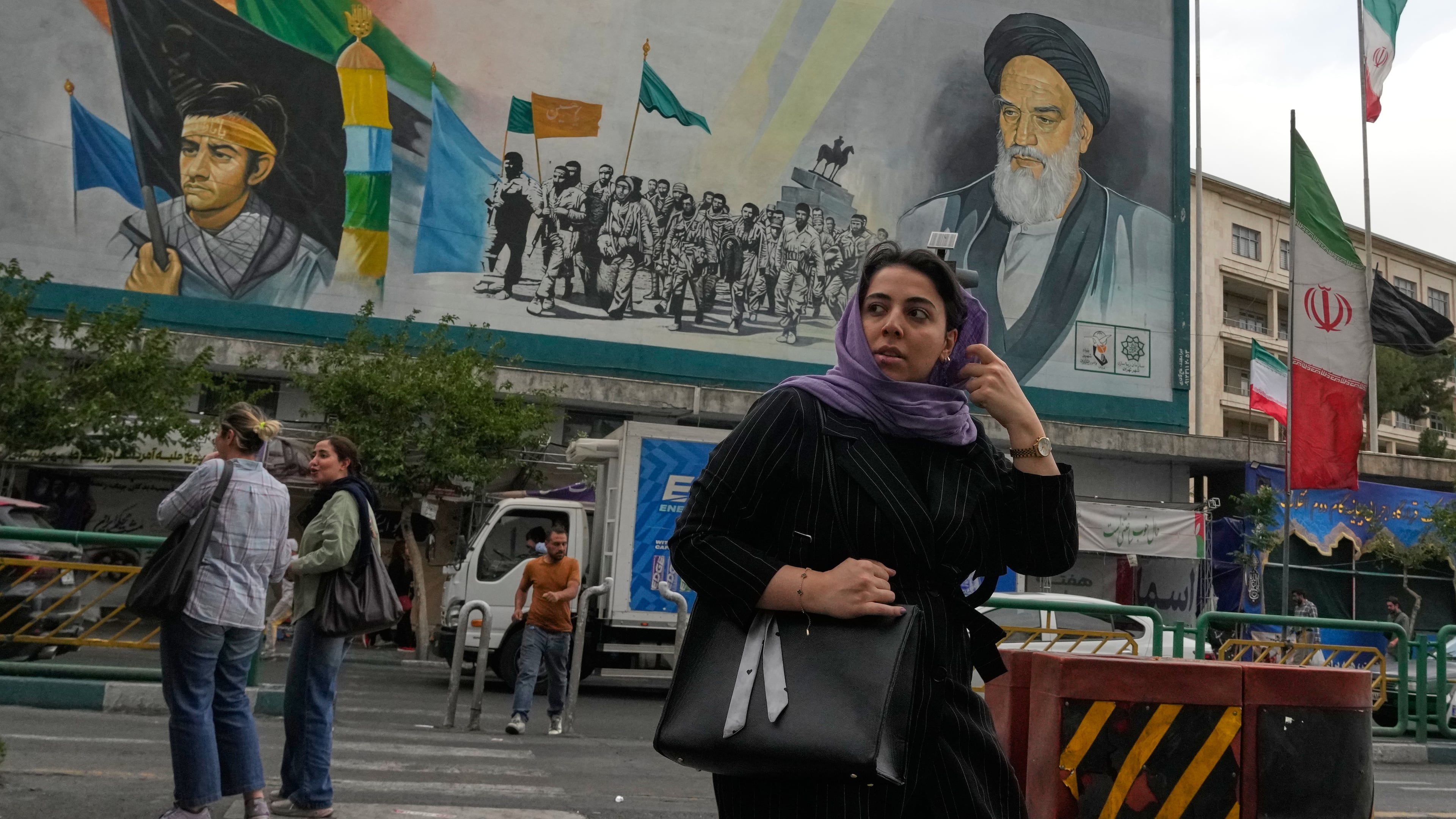 A woman crosses a street in front of a painting of the late Iranian revolutionary founder Ayatollah Khomeini and paramilitary Basij forces in downtown Tehran, Iran, Sunday, May 24, 2026. (AP Photo/Vahid Salemi)