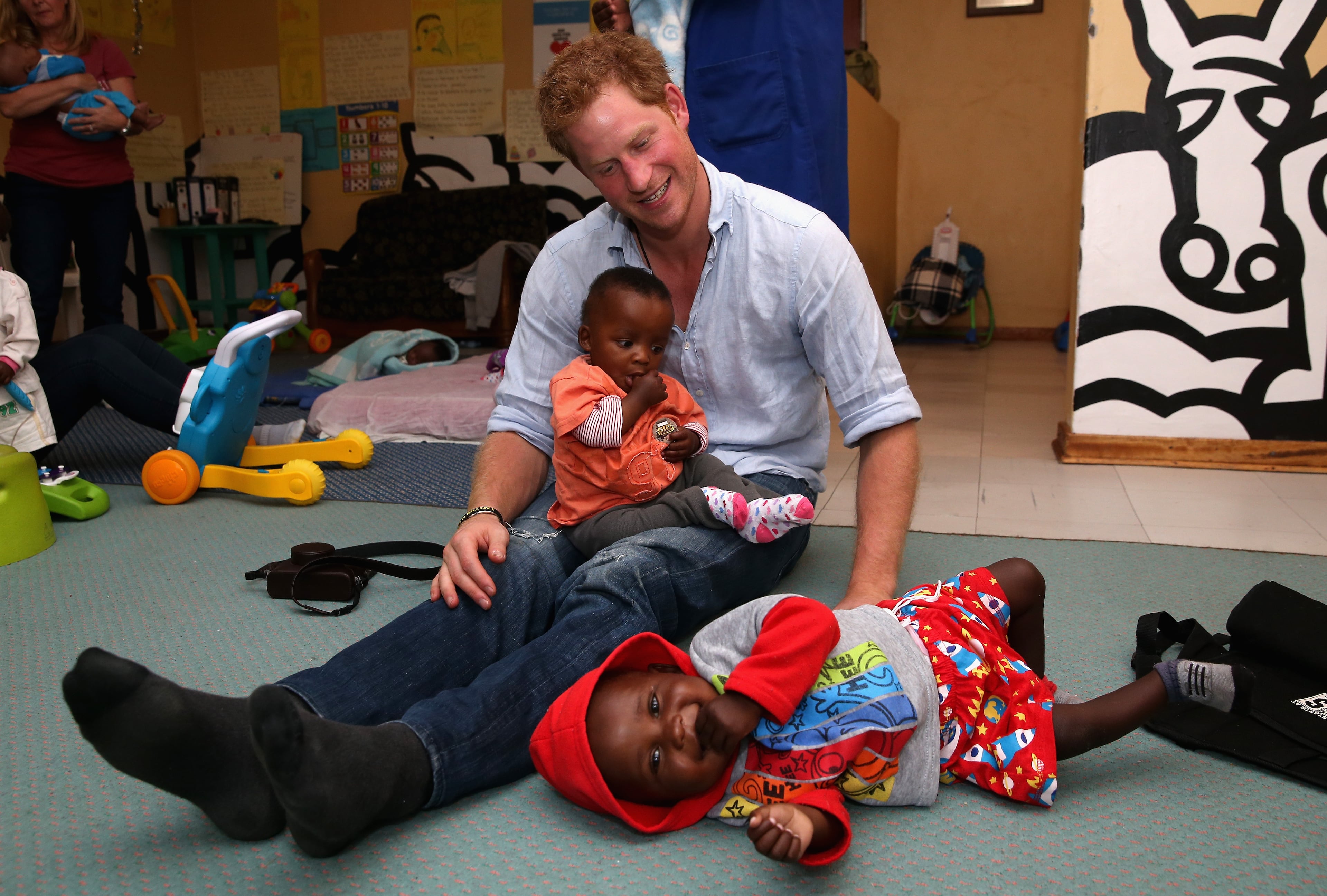 Prince Harry plays with two young children (who are going through a programme for malnourishment) during a visit to the organisation supported by Sentebale 'Touching Tiny Lives' on December 8, 2014 in Maseru, Lesotho. Prince Harry was visiting Lesotho to see the work of his charity Sentebale. Sentebale provides healthcare and education to vulnerable children in Lesotho, Southern Africa. Prince Harry said "After seeing the herd boys, we were invited back to Touching Tiny Lives in the town of Mokhotlong. There were 12 malnourished babies under the age of five that we were fortunate enough to play with for an hour. I will never forget their faces when we walked in. They only ever see and interact with women, so it took a while until they accepted us into their play pen. An enormous hail storm then hit us and two of the children had their faces pressed up against the window for about 15 minutes. These two in the picture were definitely my favorites." (Photo by Chris Jackson - WPA Pool /Getty Images)