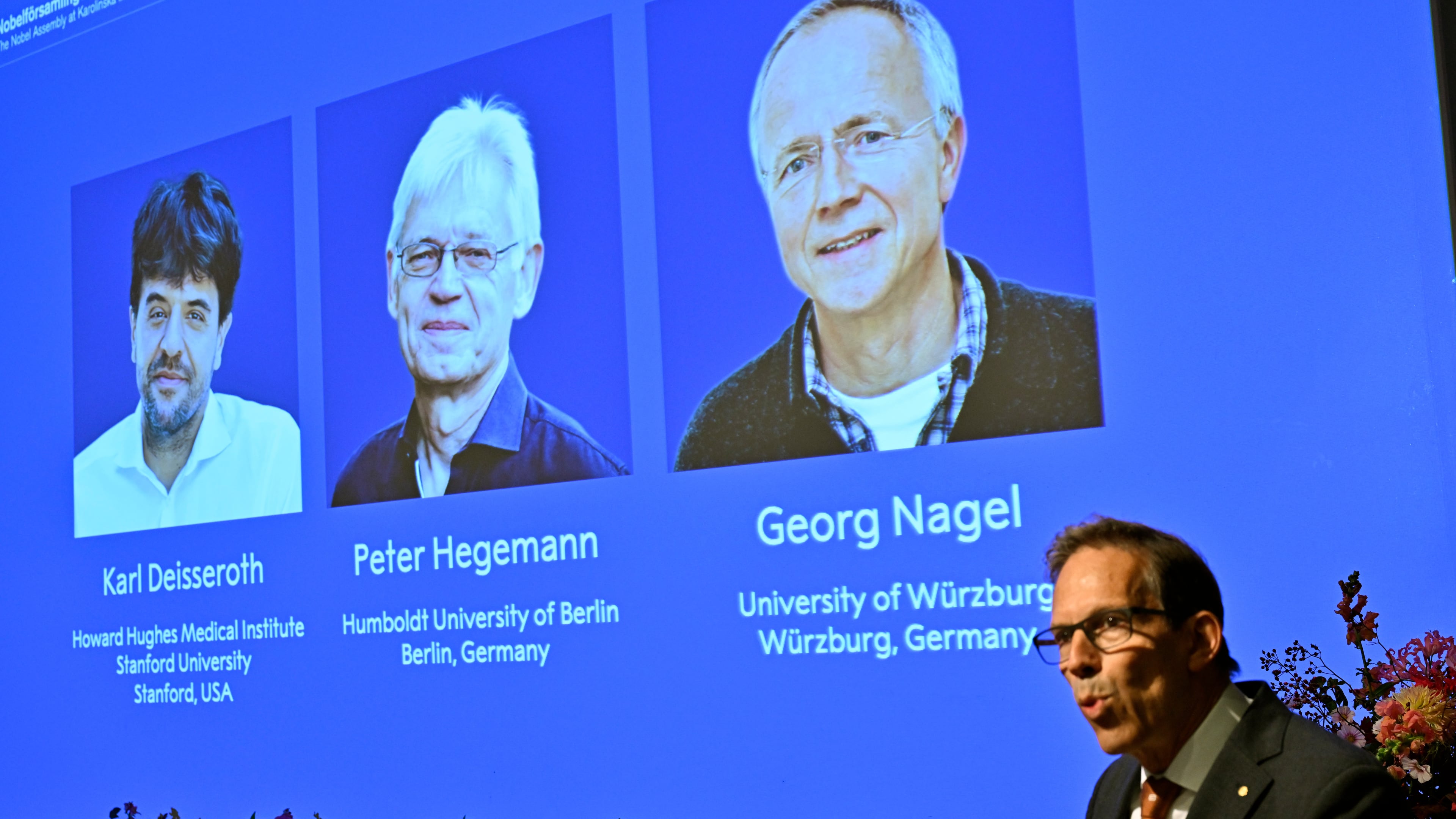 Karl Deisseroth, Peter Hegemann and Georg Nagel are shown on the screen as they are awarded the 2026 Nobel Prize in Physiology or Medicine, as announced during a press conference at the Nobel Forum at Karolinska Institutet in Stockholm, Sweden, Oct. 5, 2026. (Pontus Lundahl/TT News Agency via AP)