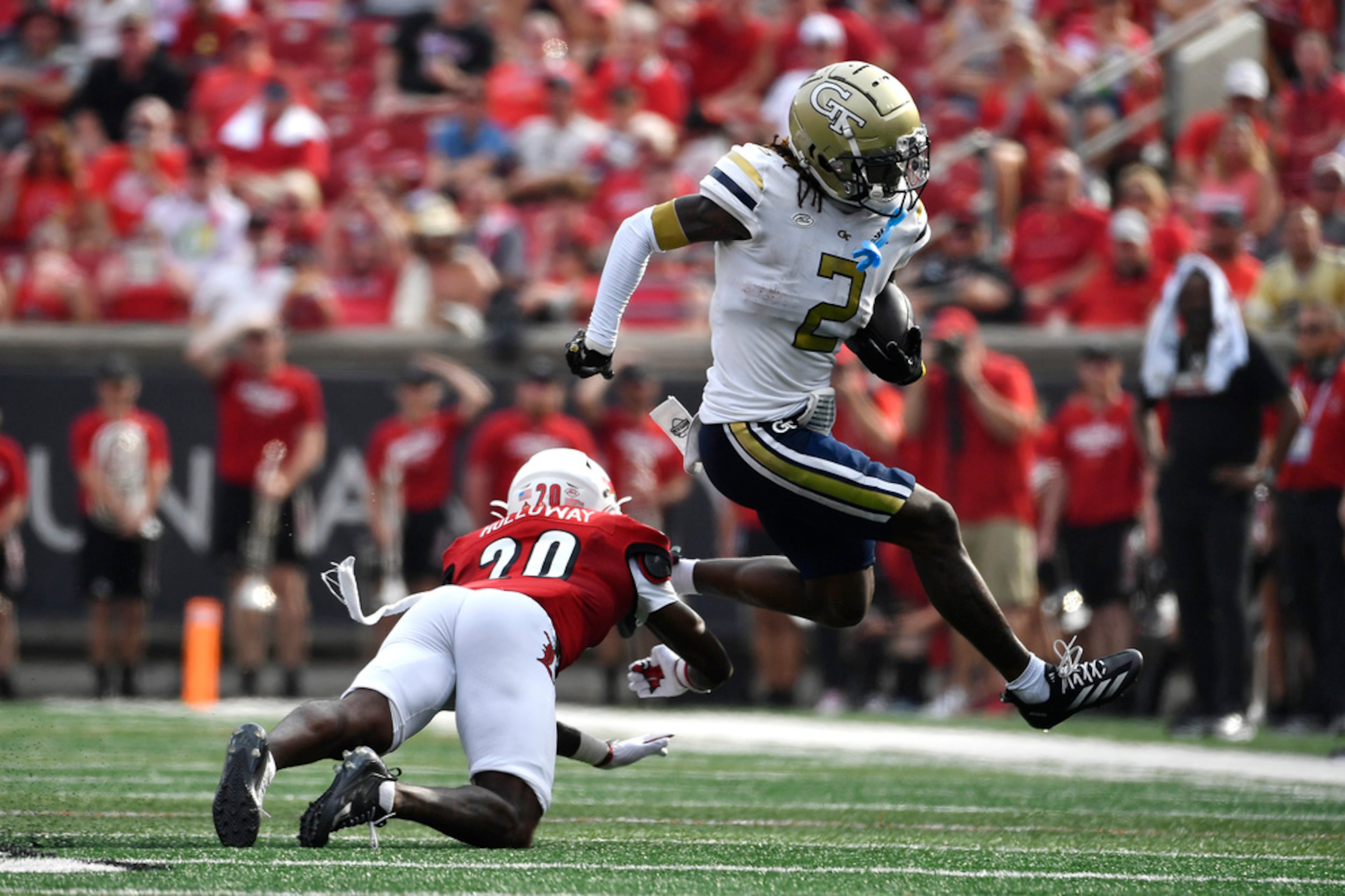 Georgia Tech wide receiver Eric Singleton Jr. (2) leaps to avoid the tackle attempt by Louisville defensive back Tayon Holloway (20) during the first half of an NCAA college football game in Louisville, Ky., Saturday, Sept. 21, 2024. (AP Photo/Timothy D. Easley)