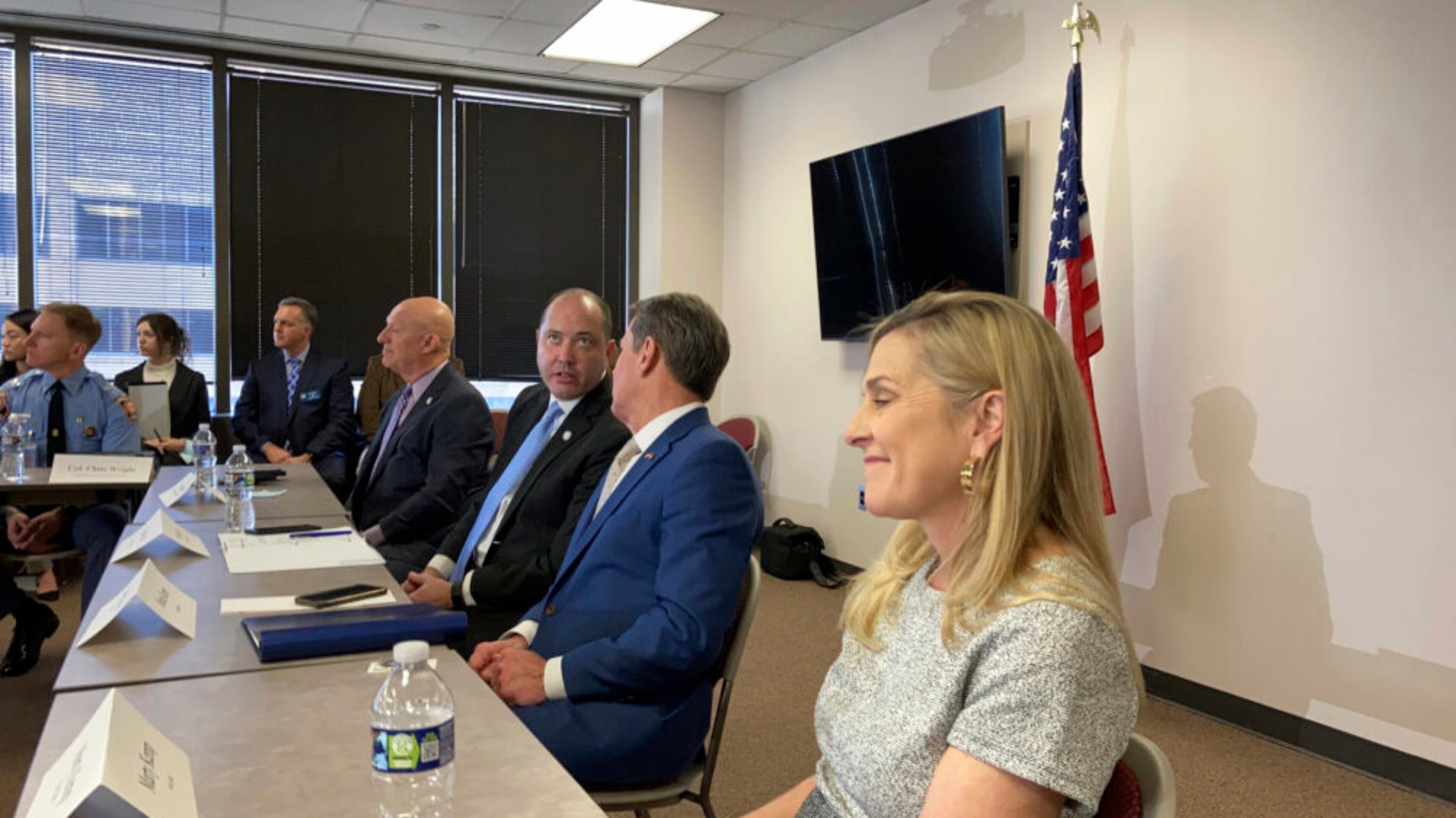 Group of men and women sitting at a table, woman smiling in the front with men talking with eachother