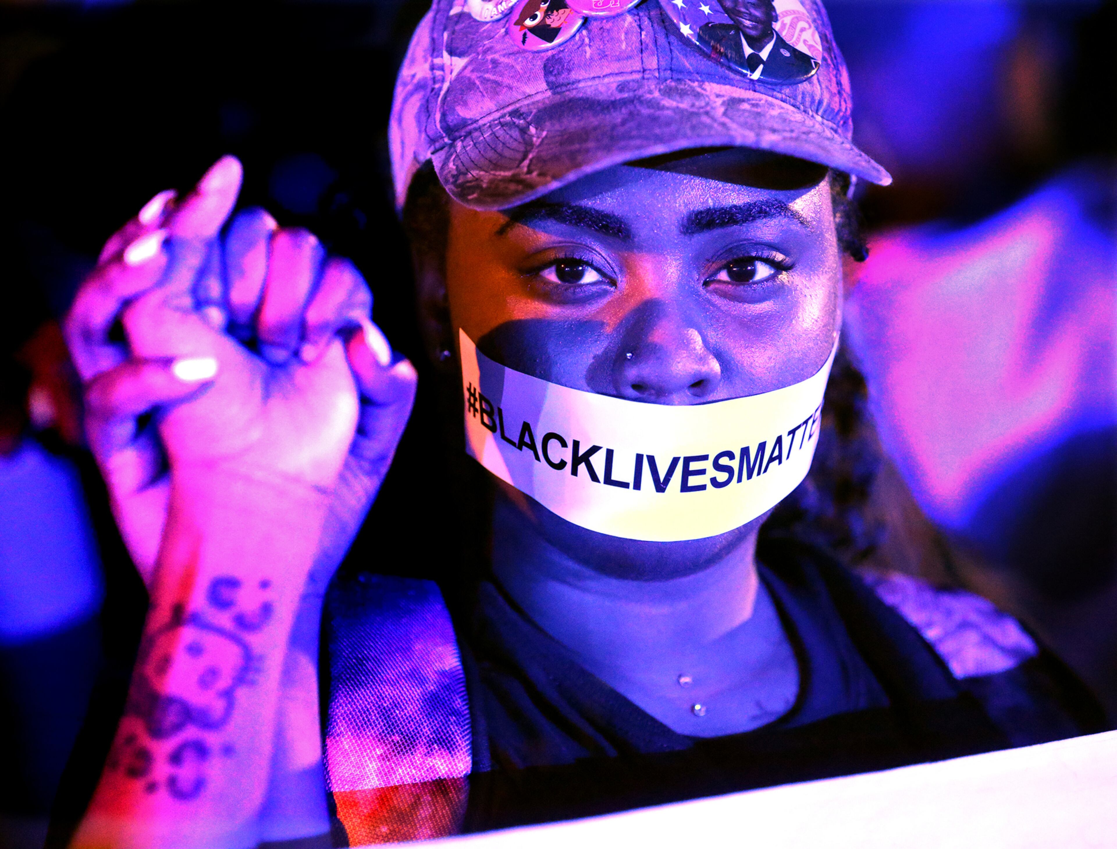 071016 ATLANTA: A woman light by the lights of police vehicles joins hands in silent protest across from the Governor's mansion with a Black Lives Matter sticker over her mouth during a fifth night of demonstrations on Monday, July 11, 2016, in Atlanta. Curtis Compton /ccompton@ajc.com