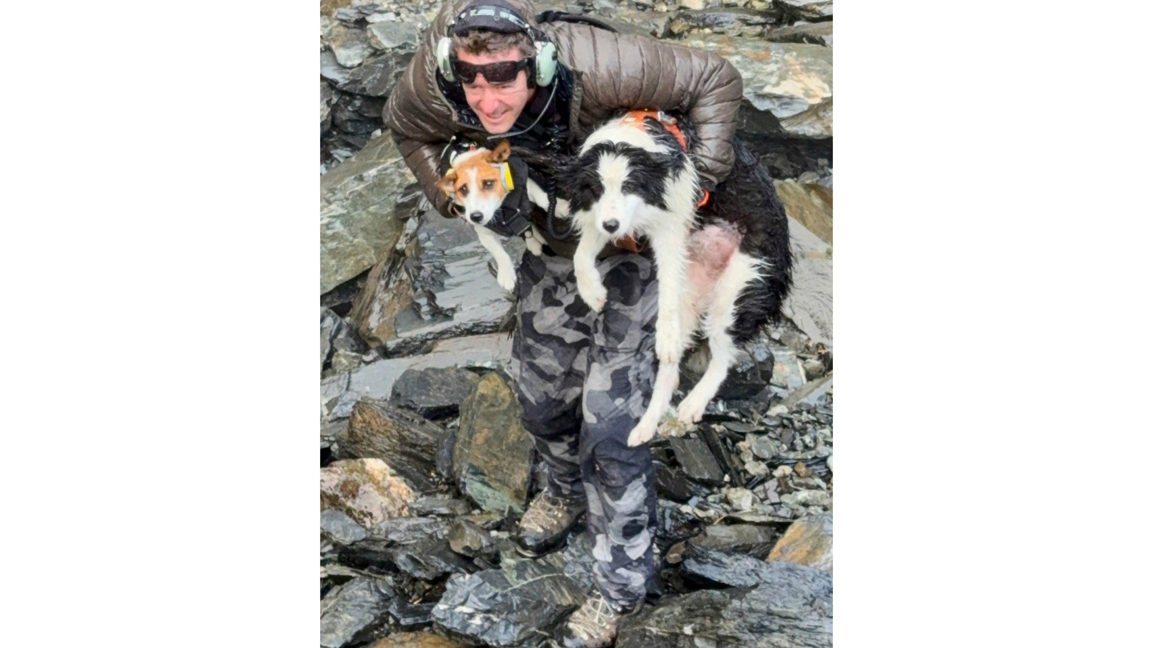 In this photo released by Precision Helicopters Ltd, Wayne Holmes holds his dog Bingo, left, after the rescue of Molly, right, at a waterfall on the Arahura River on the West Coast of the South Island of New Zealand, Tuesday, March 31, 2026. (Precision Helicopters Ltd via AP)