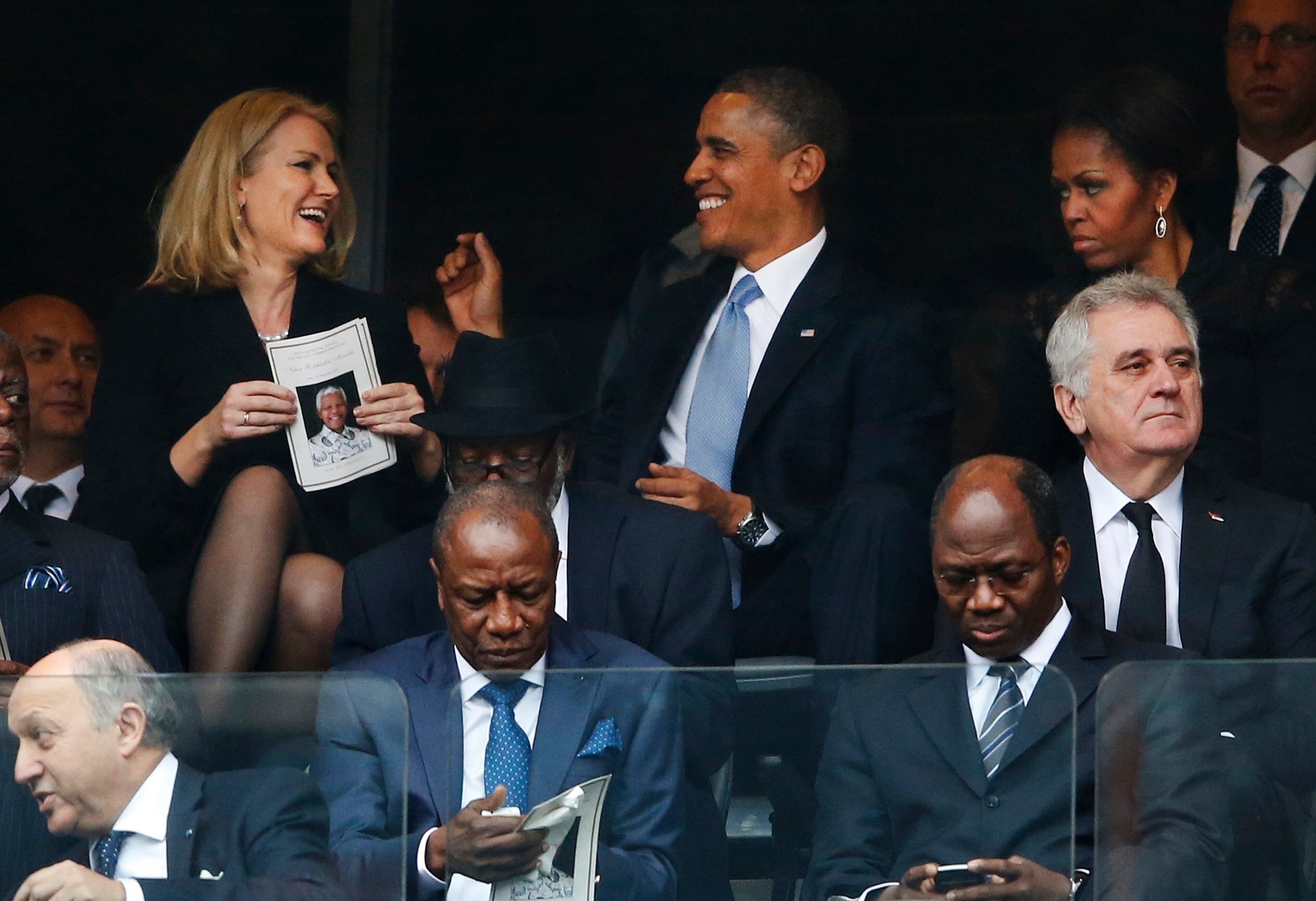 President Barack Obama jokes with Danish prime minister, Helle Thorning-Schmidt, left, as first lady Michelle Obama looks on at right during the memorial service for former South African president Nelson Mandela at the FNB Stadium in Soweto, near Johannesburg, South Africa, Tuesday Dec. 10, 2013. (AP Photo/Matt Dunham)