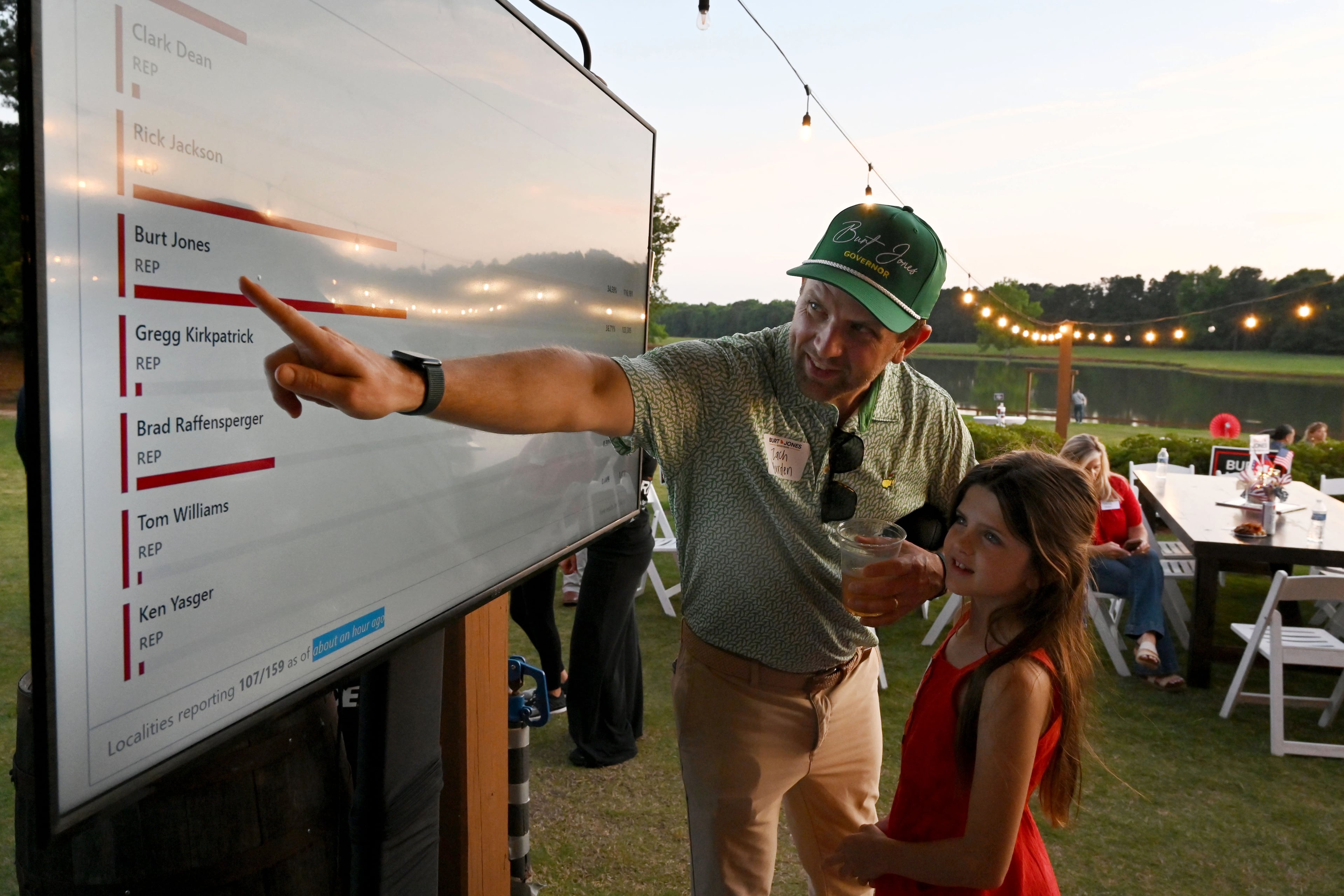 Zach Burden, with his daughter Parker, monitors poll results during an election night party for Georgia gubernatorial candidate Burt Jones at The Rivers Ranch on Tuesday in Jackson. (Hyosub Shin/AJC)