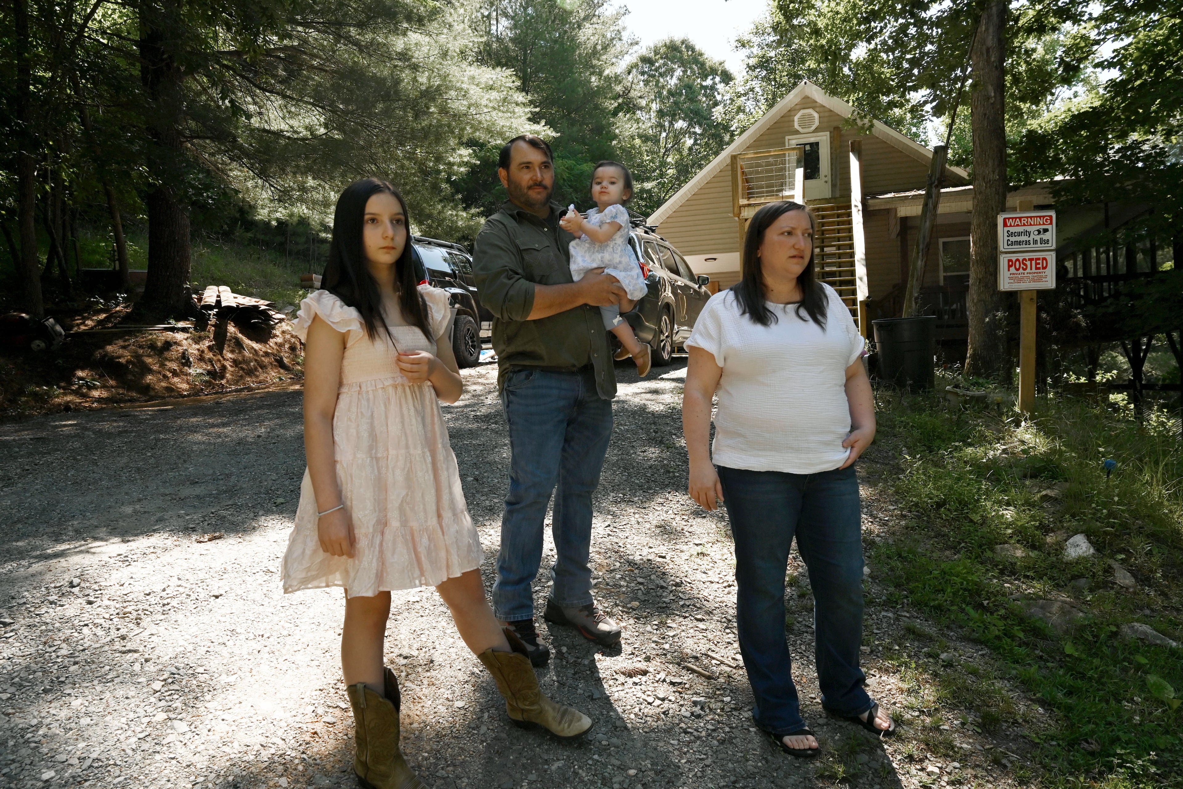 Kristy Guarnieri (right) and husband Courtney Guarnieri stand with their daughters, Stella, 12 (left) and Eliza, 1, on their property in Morganton in North Georgia on Thursday, June 4, 2026. They say their lives have been upturned by animals getting loose from the nearby Hooves and Feathers Petting Farm. (Hyosub Shin/AJC)
