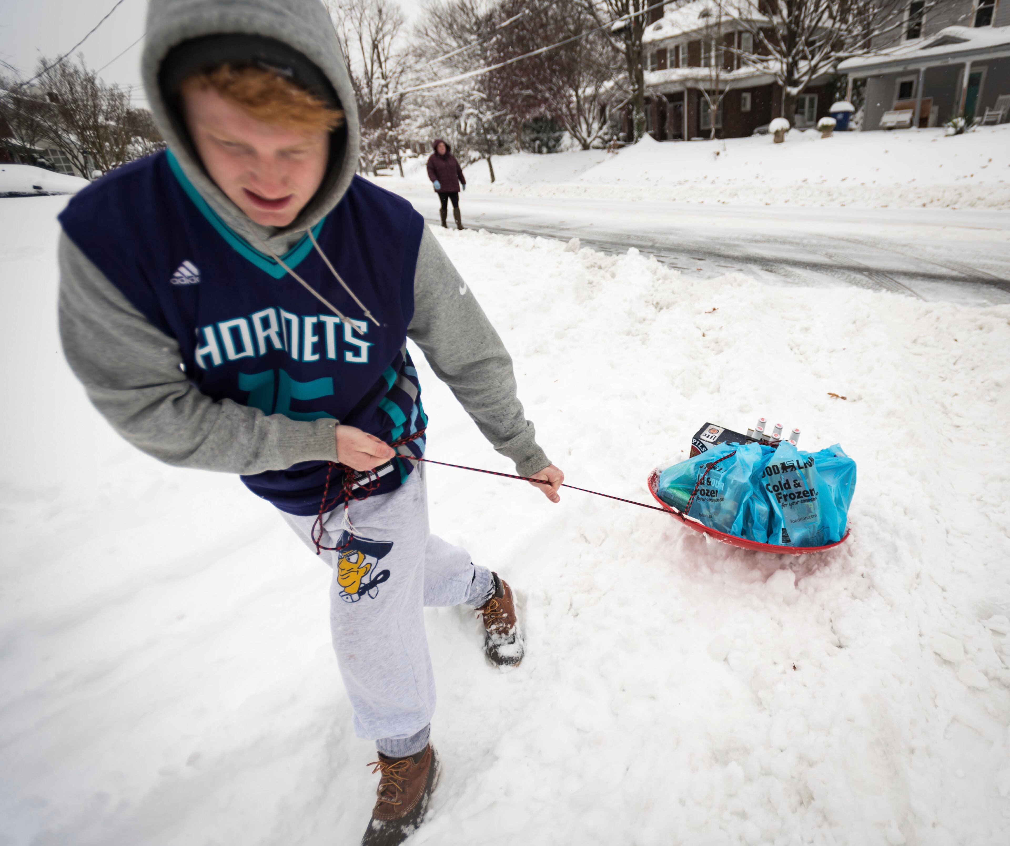 Daniel Havens, 18, struggles to pull a sled full of groceries tied to his waist as he turns onto the unplowed Ebert Road from South Hawthorne Road with his mother Susan Havens and sister Maddie Havens on Sunday, Dec. 9, 2018, in Winston-Salem, N.C. (Allison Lee Isley/The Winston-Salem Journal via AP)
