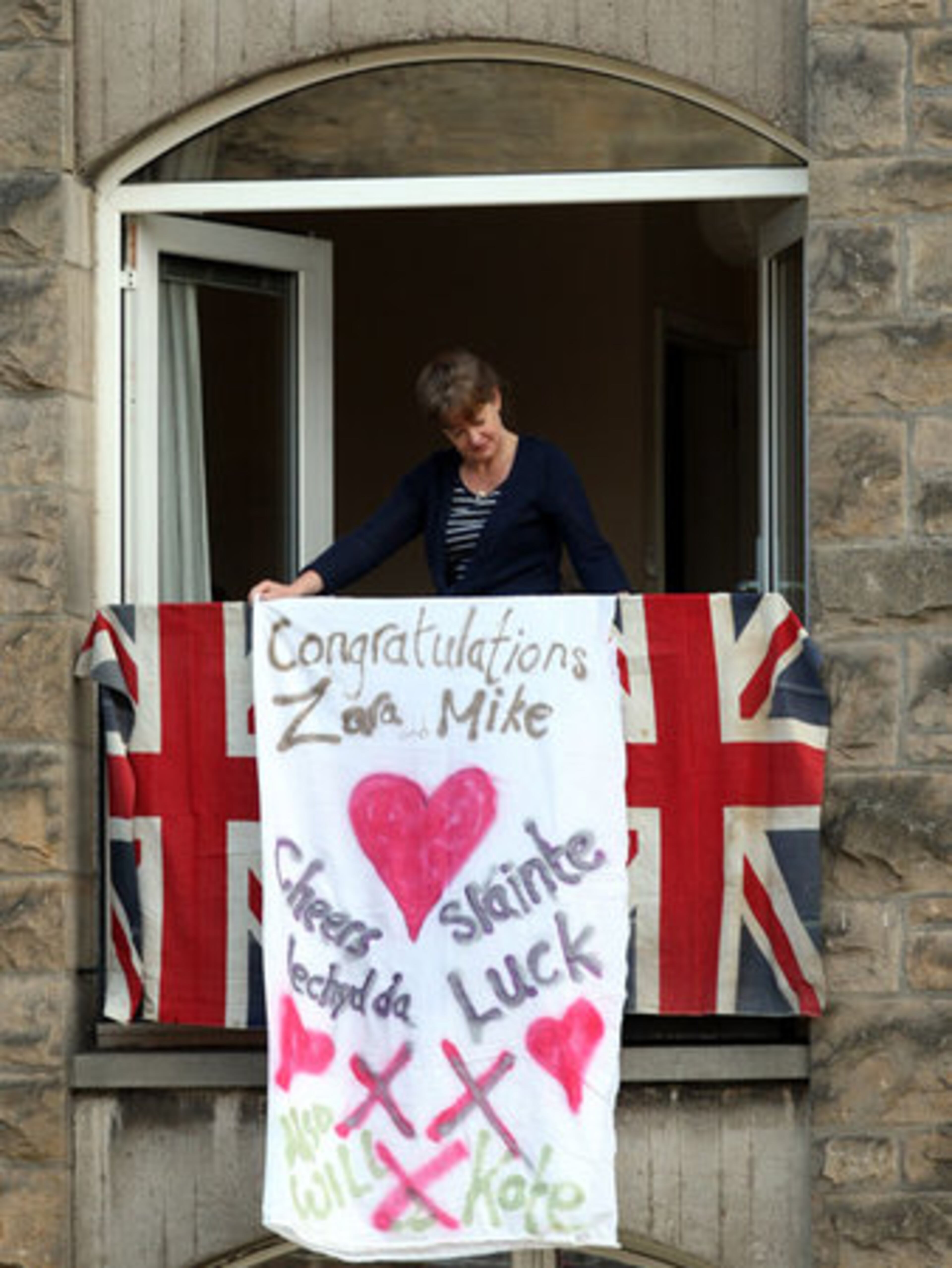 A woman looks from her balcony festooned with Union flags and a banner for the wedding of equestrian star Zara Phillips and Mike Tindall.