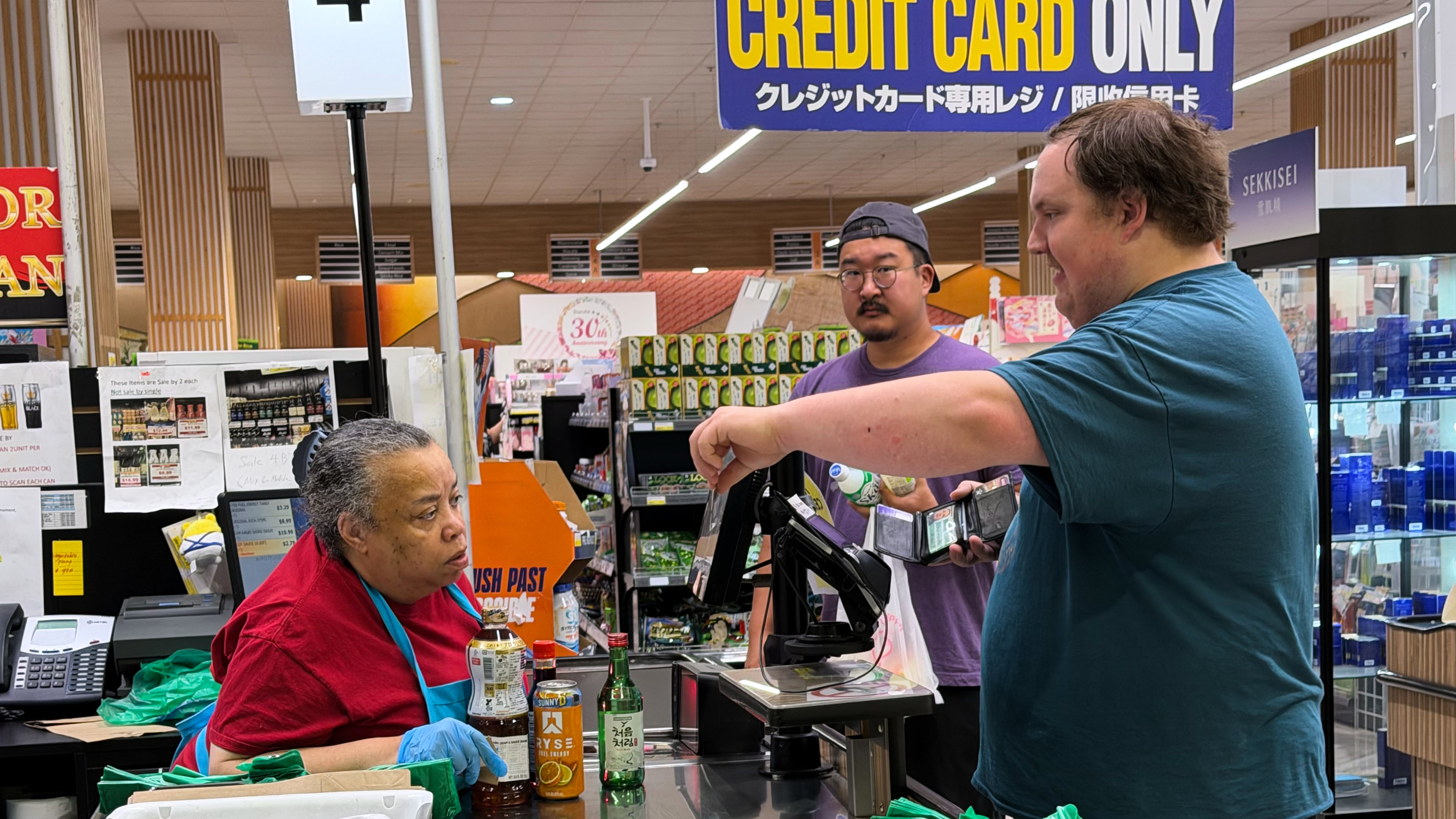 An employee checks a customer's identification card before checking out alcohol at a cash register in a grocery store in Arlington Heights, Ill., Monday, July 6, 2026. (AP Photo/Nam Y. Huh)