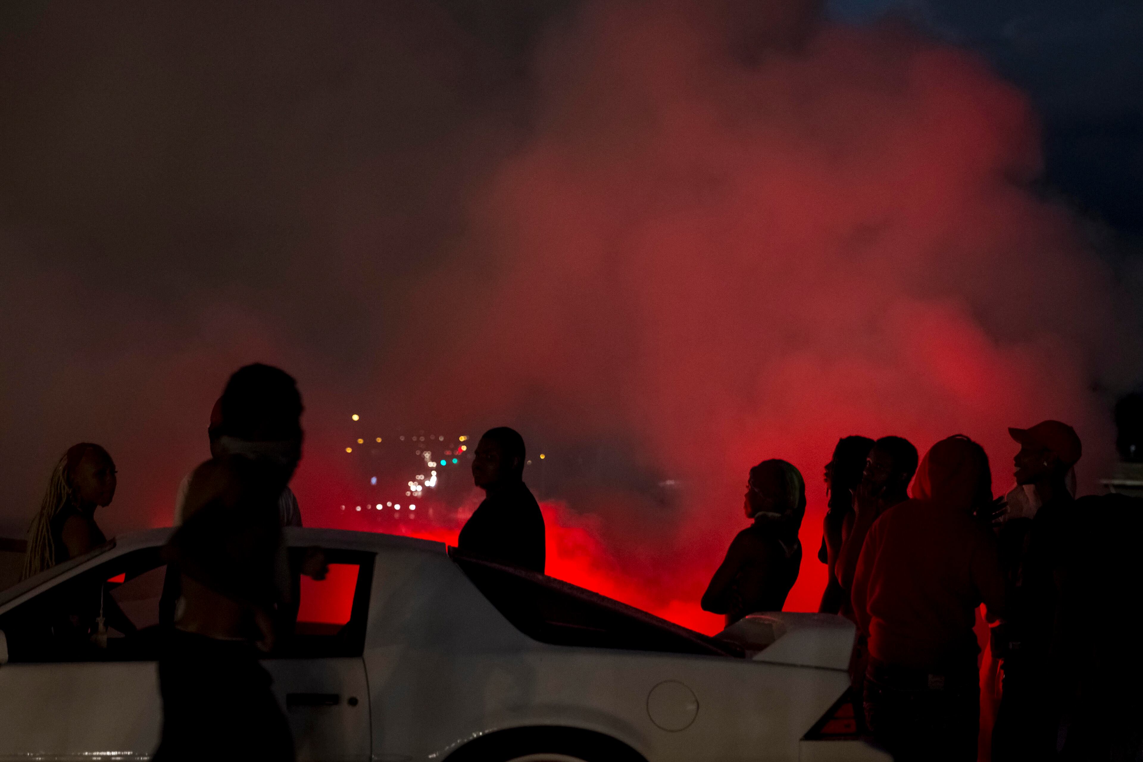 A driver burns out their tires as people watch protesters marching down West Florissant Avenue in Ferguson, Mo., Aug. 9, 2015. A day of peaceful protest commemorating the killing of an unarmed black teenager by a white police officer one year ago ended in gunfire late Sunday. A St. Louis County police officer was involved in the shooting, the department said. (Whitney Curtis/The New York Times)