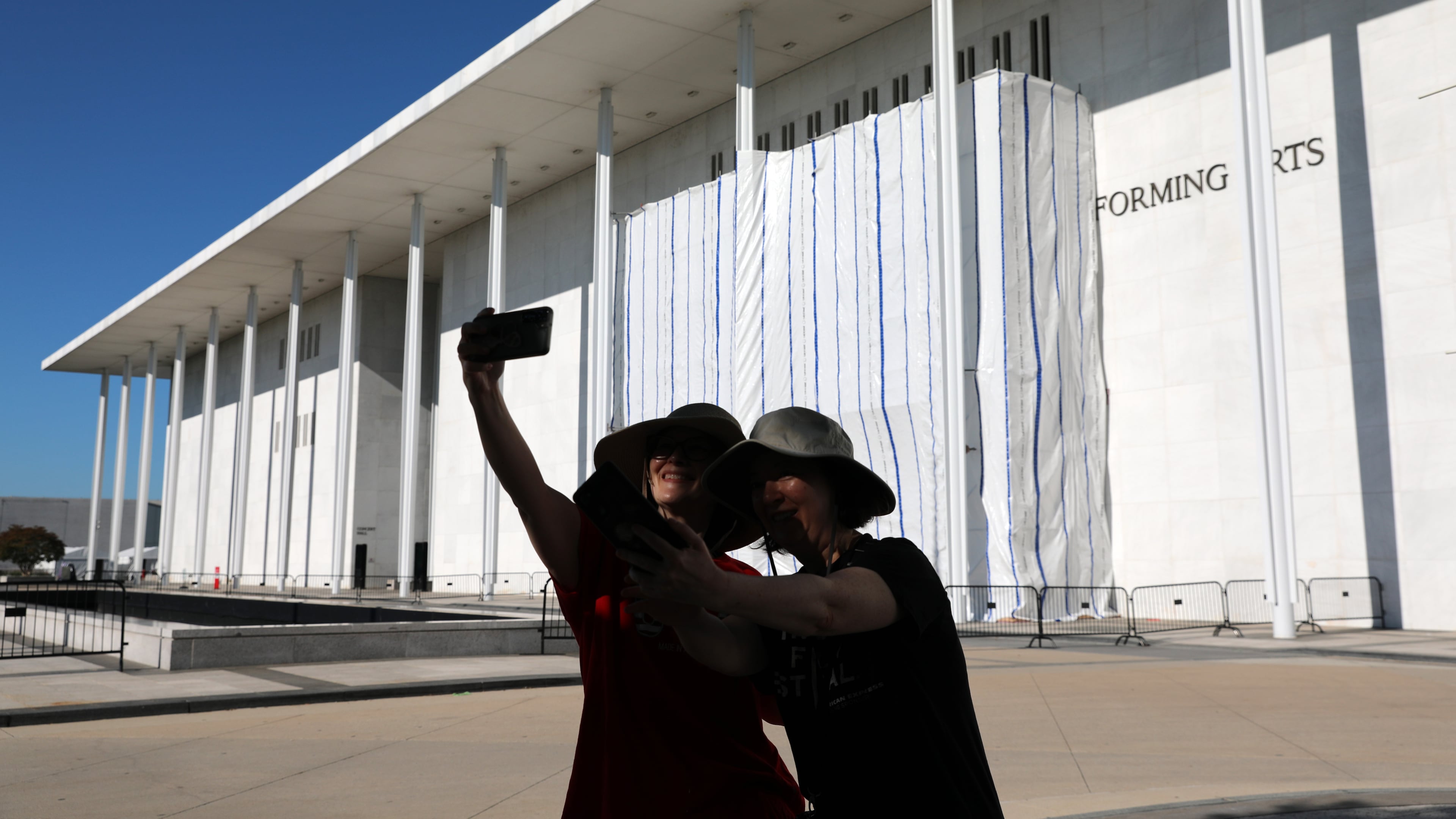 Women take a selfie as the wall of the John F. Kennedy Center for the Performing Arts is covered in tarp as work continues on the removal of President Donald Trump's name, Saturday, June 13, 2026 in Washington. (AP Photo/Rahmat Gul)
