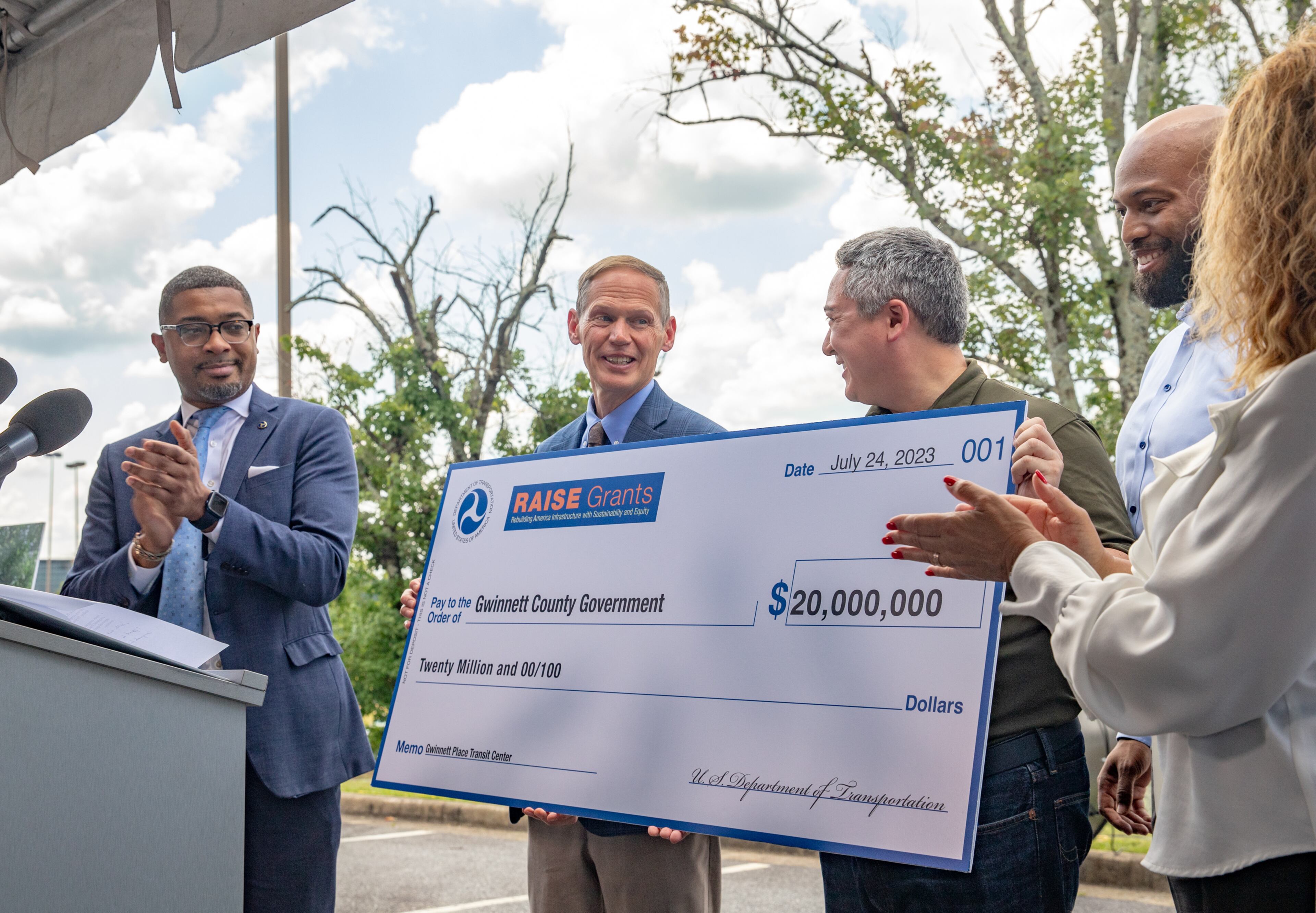 Assistant Secretary of Transportation Christopher Coes, from left, participates with Lewis Cooksey, director of the Gwinnett Department of Transportation, and Ben Ku and others in the ceremonial check presentation of a $20 million federal grant Monday, July 24, 2023 awarded to transform the transit center just west of Gwinnett Place Mall. (Jenni Girtman for The Atlanta Journal-Constitution)