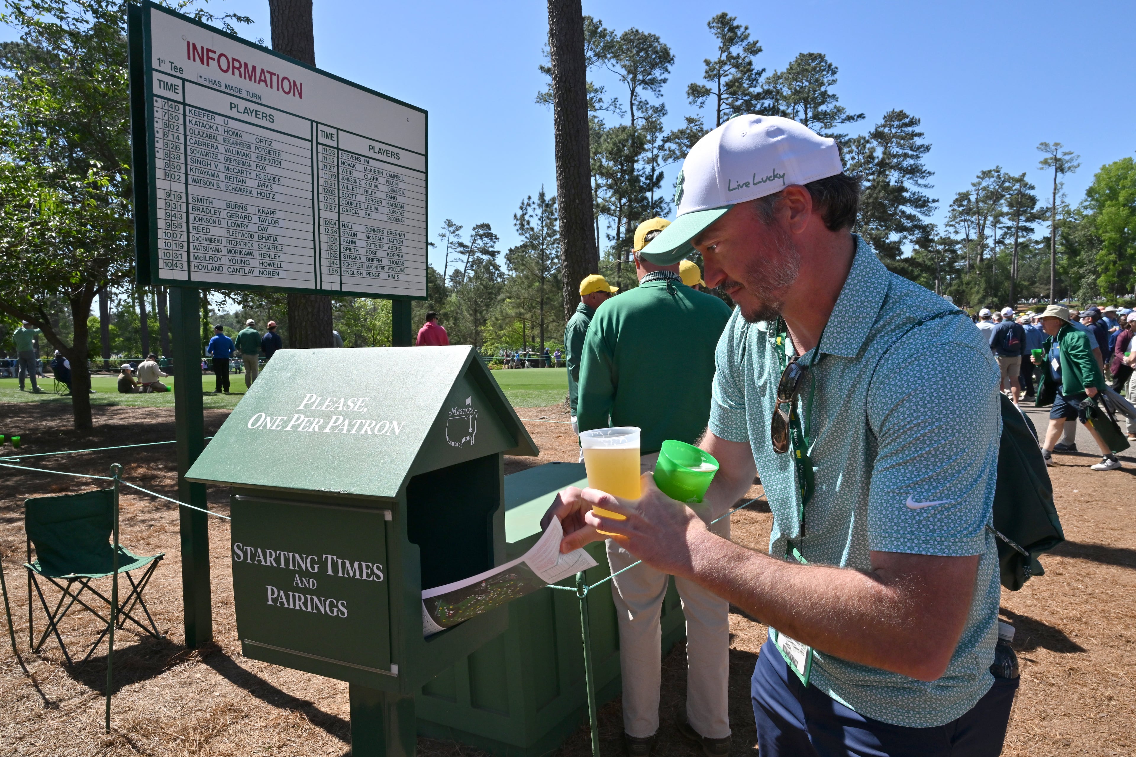 A patron grabs a pairing sheet during the first round of the Masters on Thursday. With no screens or cellphones allowed, Augusta National provides the pairing sheets. (Hyosub Shin/AJC)