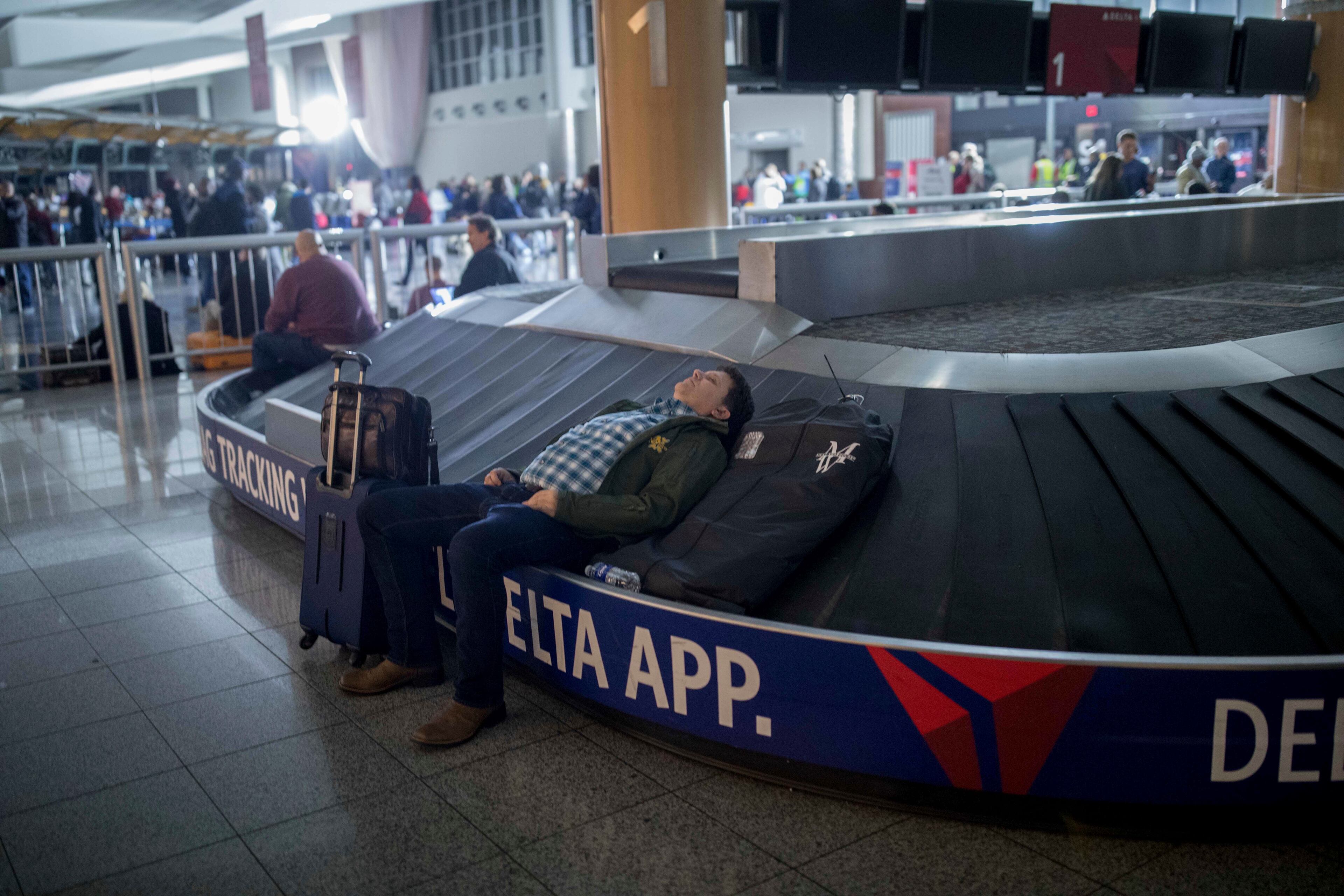 A traveler sleeps on a baggage carousel at Hartfield-Jackson Atlanta International Airport, Sunday, Dec. 17, 2017, in Atlanta. A sudden power outage at the airport on Sunday grounded scores of flights and passengers during one of the busiest travel times of the year. (AP Photo/Branden Camp)