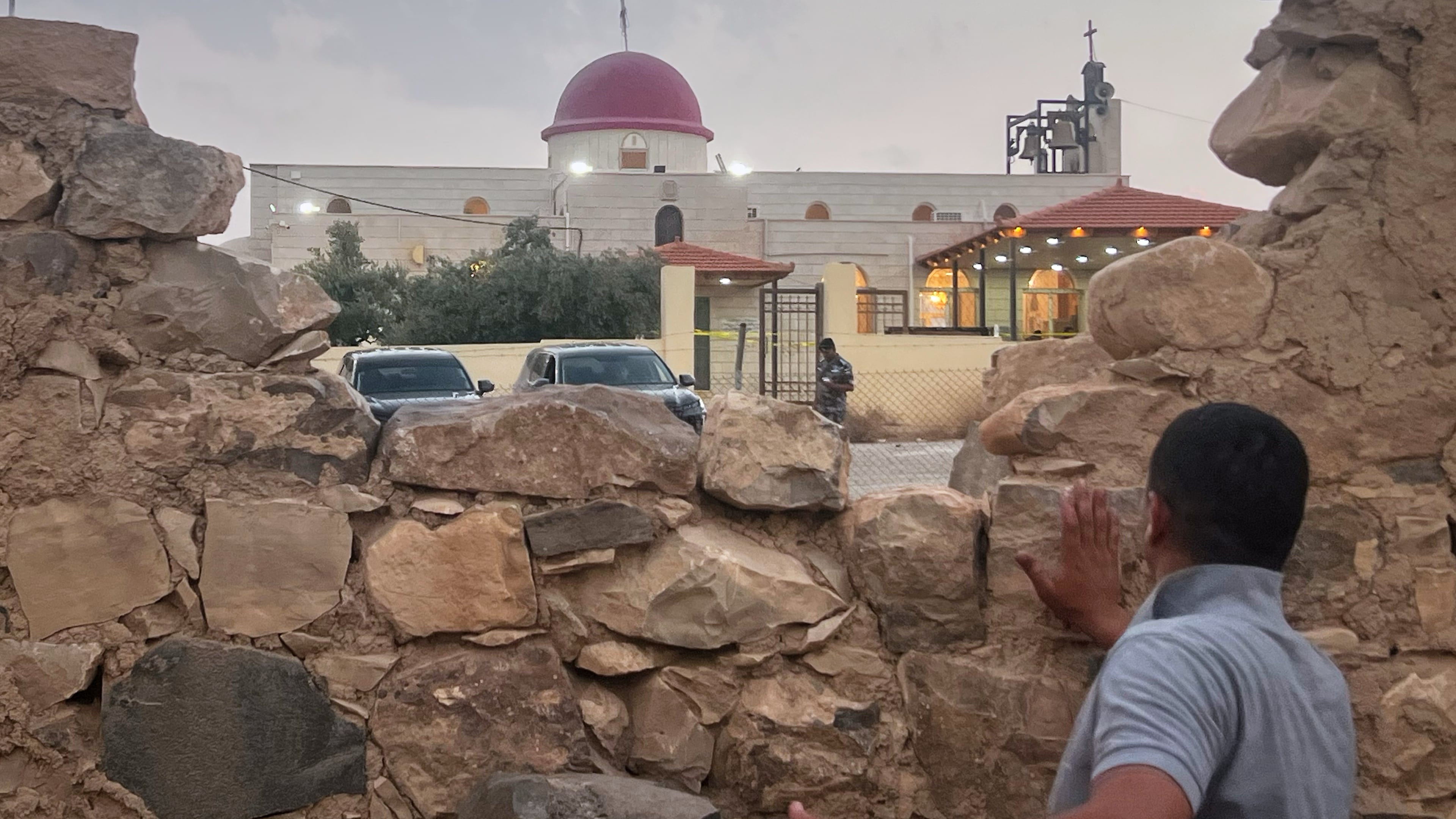 A man looks through a gap in a stone wall toward a Greek Orthodox church where gunmen opened fire during a funeral hours earlier in Hamoud village, in Jordan's Karak governorate, Friday, Oct. 23, 2026. (AP Photo)