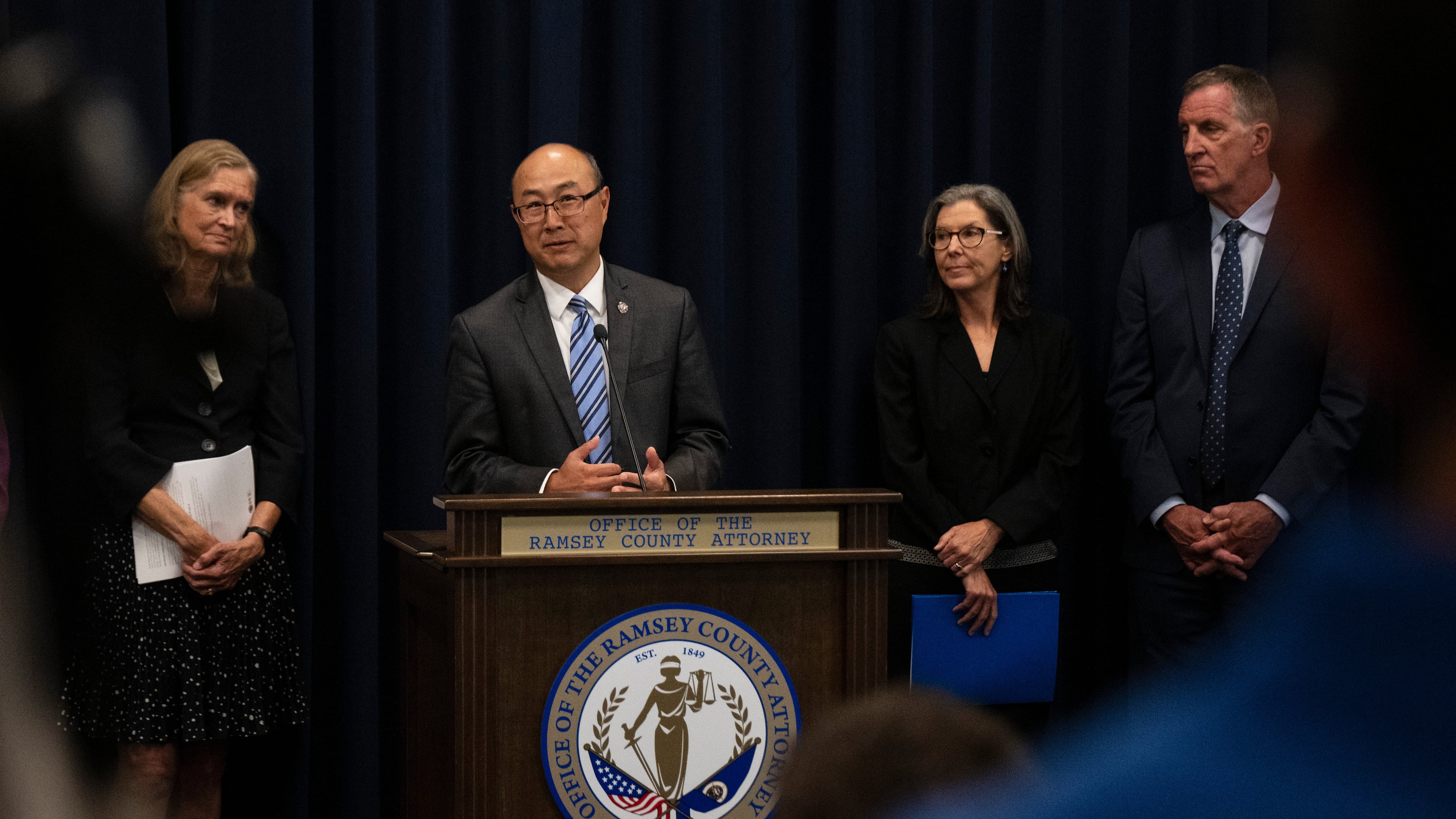 FILE - Ramsey County Attorney John Choi, at podium, discusses his office's review of former Ramsey County Medical Examiner Michael McGee's work during a news conference in St. Paul, Minn., Sept. 11, 2024.(John Autey/Pioneer Press via AP, File)