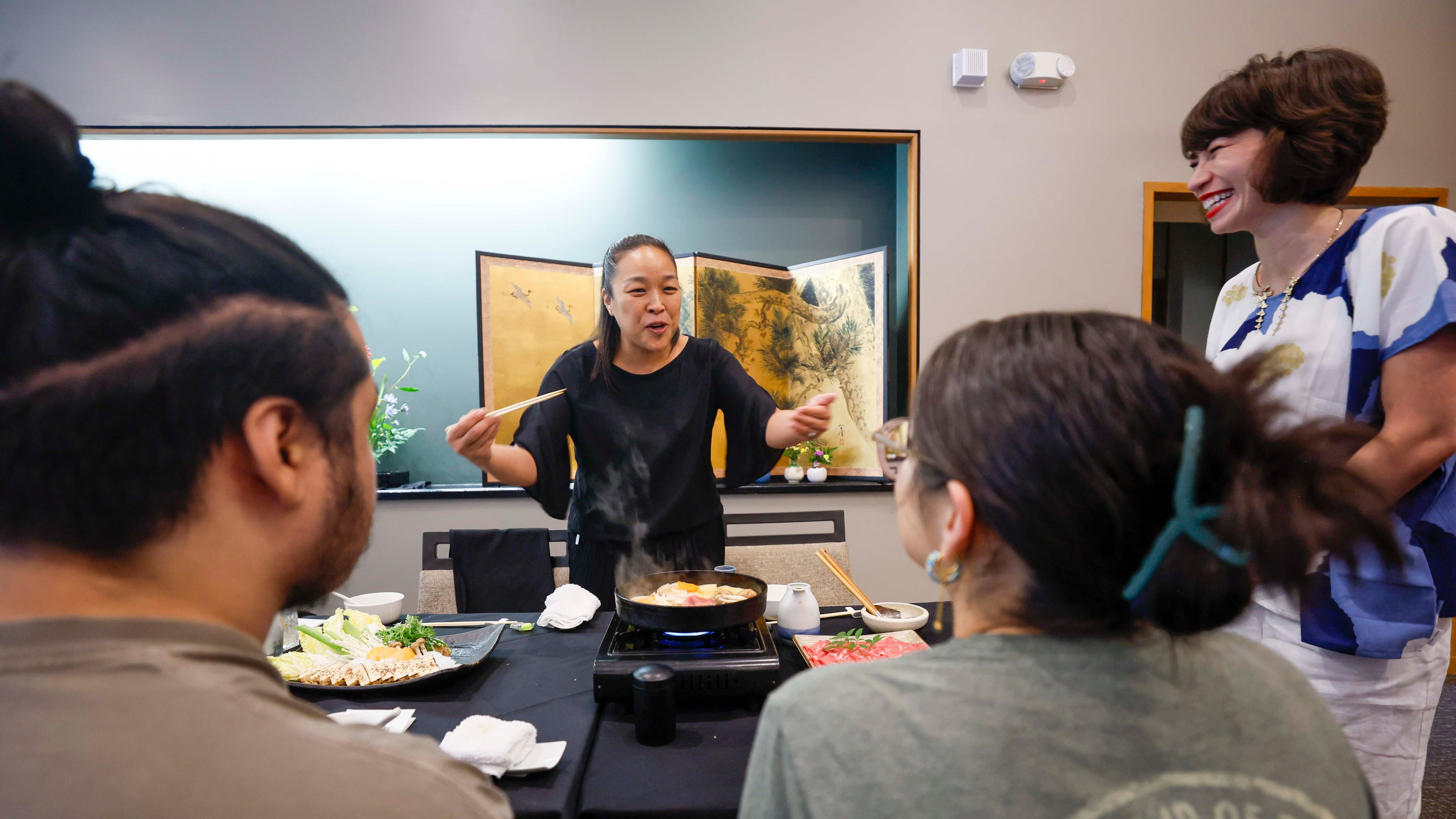 Sachiyo Nakato Takahara, owner of Nakato Japanese Restaurant, happily explains to students what the “Sukiyaki” dish is made of as Freedom University executive director Laura Emiko Soltis looks on during a celebratory dinner at Nakato restaurant in Atlanta on Sunday, Aug. 23, 2026, marking the conclusion of the virtual study abroad Japan program. (Miguel Martinez/AJC)
