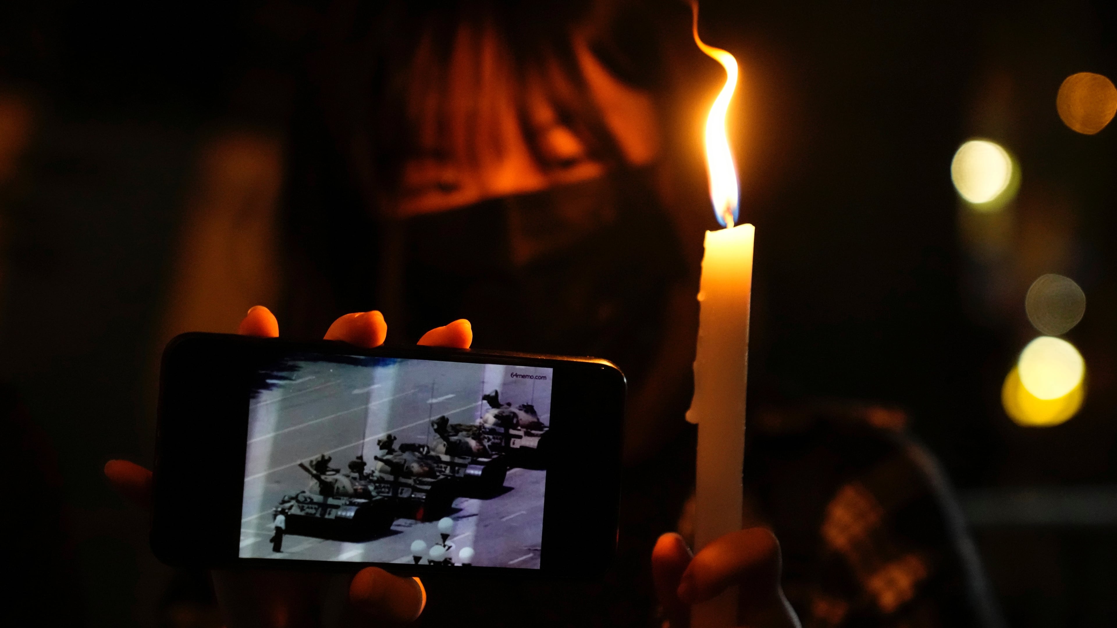 FILE -A woman holds up a candle and an image of a man facing off tanks to mark the anniversary of the military crackdown on a pro-democracy student movement in Beijing, during a light candle vigil outside Victoria Park in Hong Kong, Friday, June 4, 2021. (AP Photo/Kin Cheung, File, File)