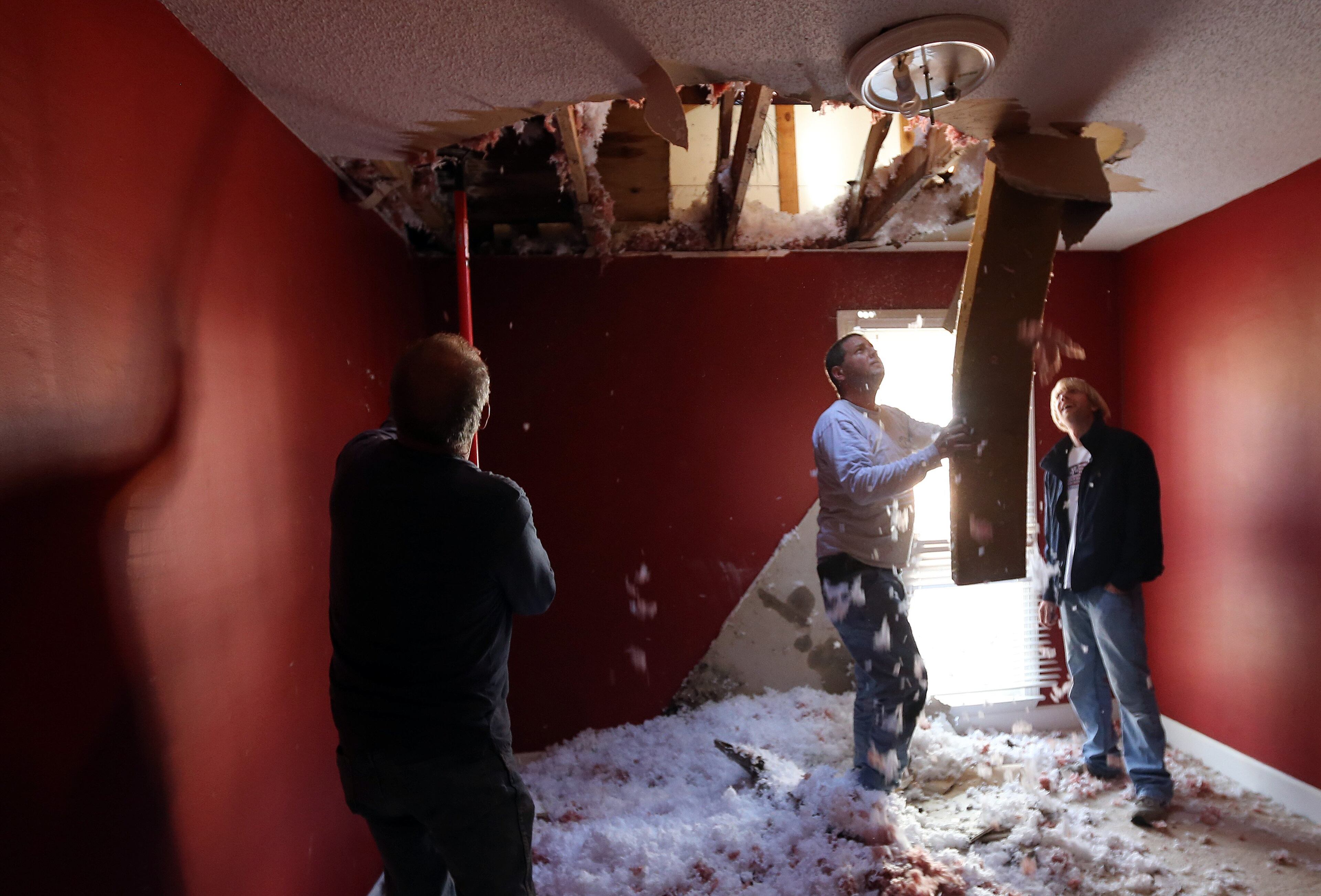 Spencer Pearson, right, watches Mike and Mitchell Amerson rip damaged sections of ceiling out of his guest room Saturday morning February 15, 2014 after an ice-covered pine tree snapped and speared through the roof and ceiling and ended up embedded in the floor of the room. Pearson was staying at his girlfriend's house when the tree fell, so nobody was hurt. BEN GRAY / BGRAY@AJC.COM