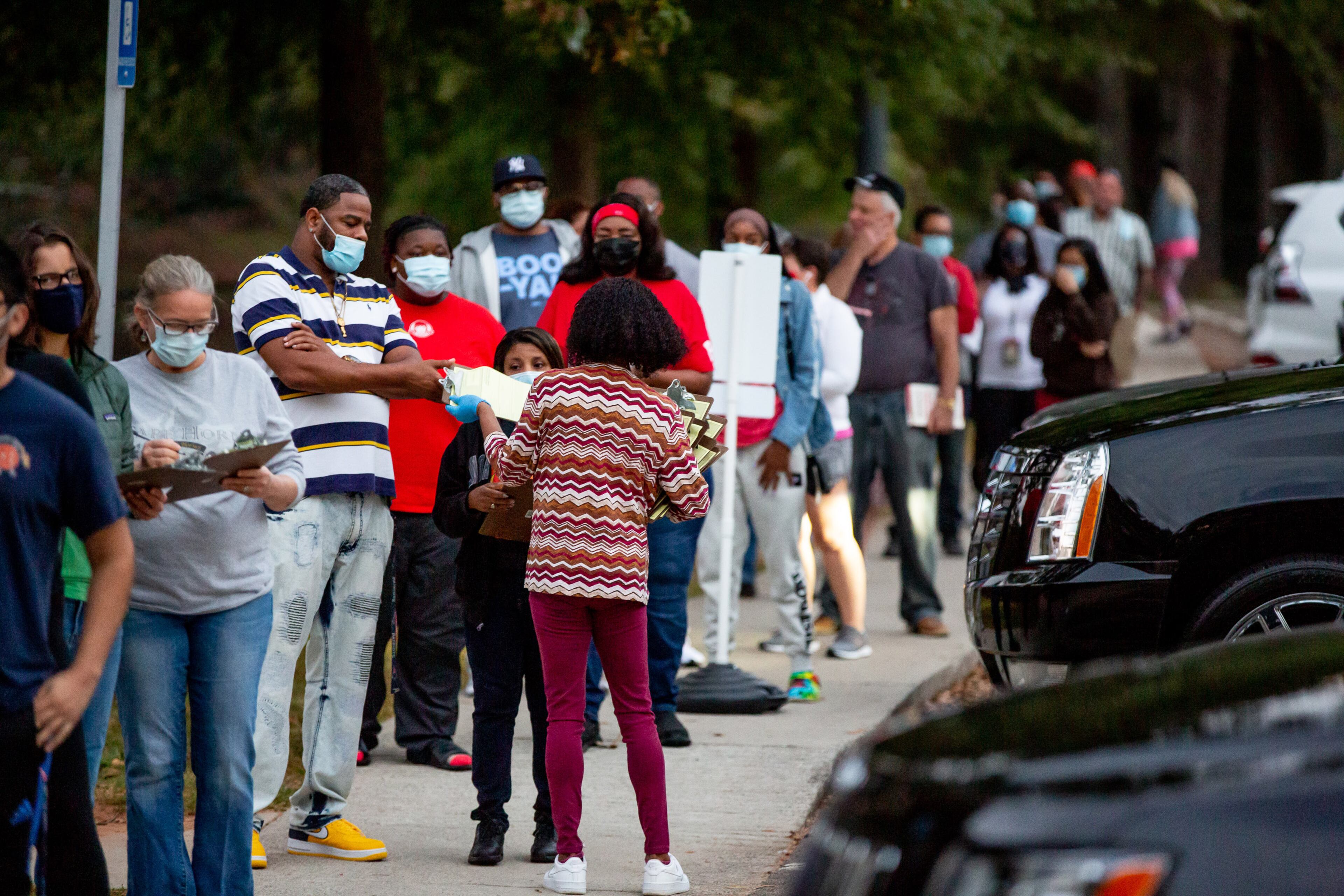 People fill out forms while waiting in line to vote at Shorty Howell Park in Gwinnett on Saturday, October 24, 2020. STEVE SCHAEFER / SPECIAL TO THE AJC