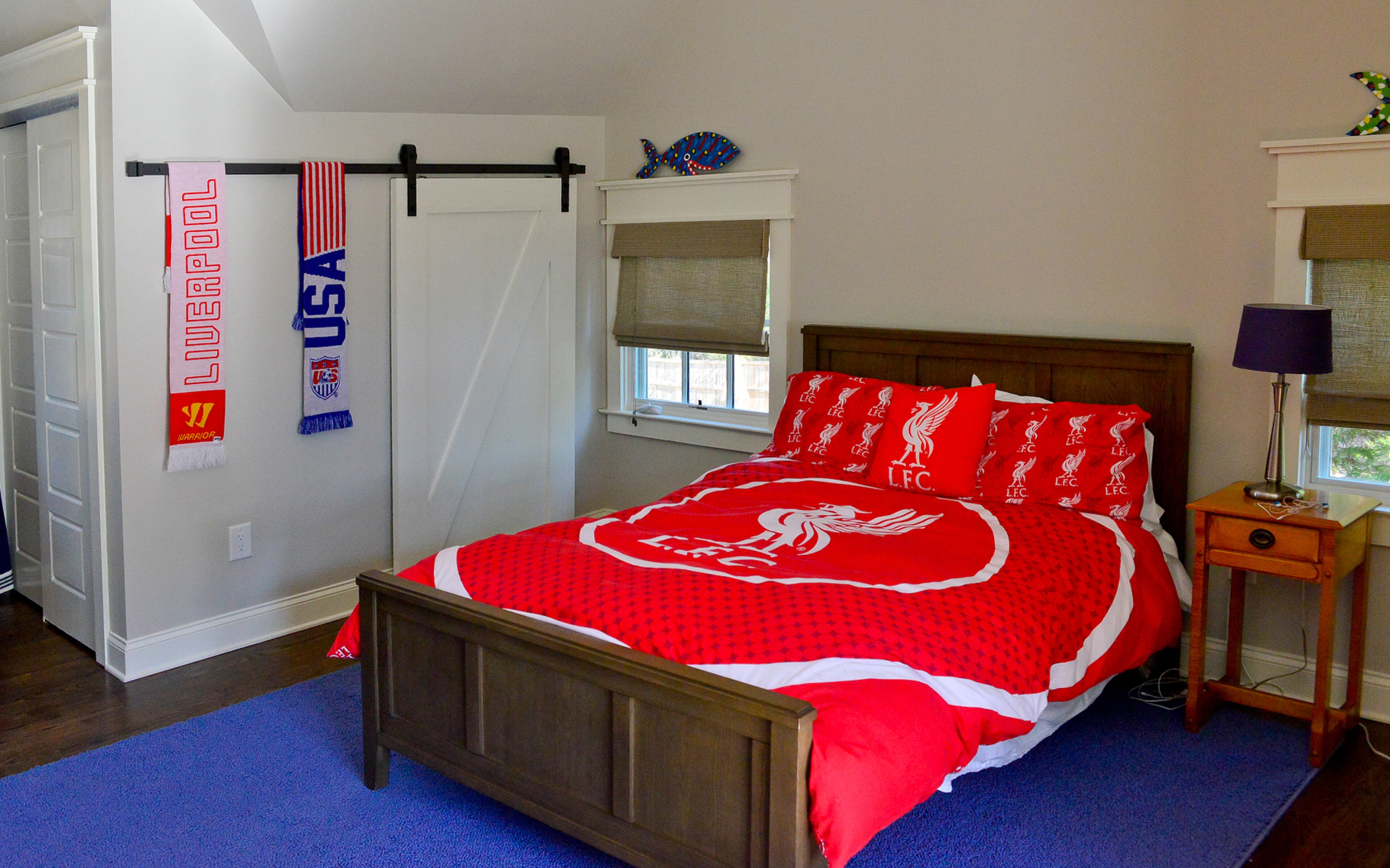 Kieran Bailey's spacious bedroom includes several built-in storage areas. A blue rug complements the middle-schooler's bright red Liverpool Football Club comforter, while the barn door's sliding rail gives him extra hanging space to display more soccer fan gear.